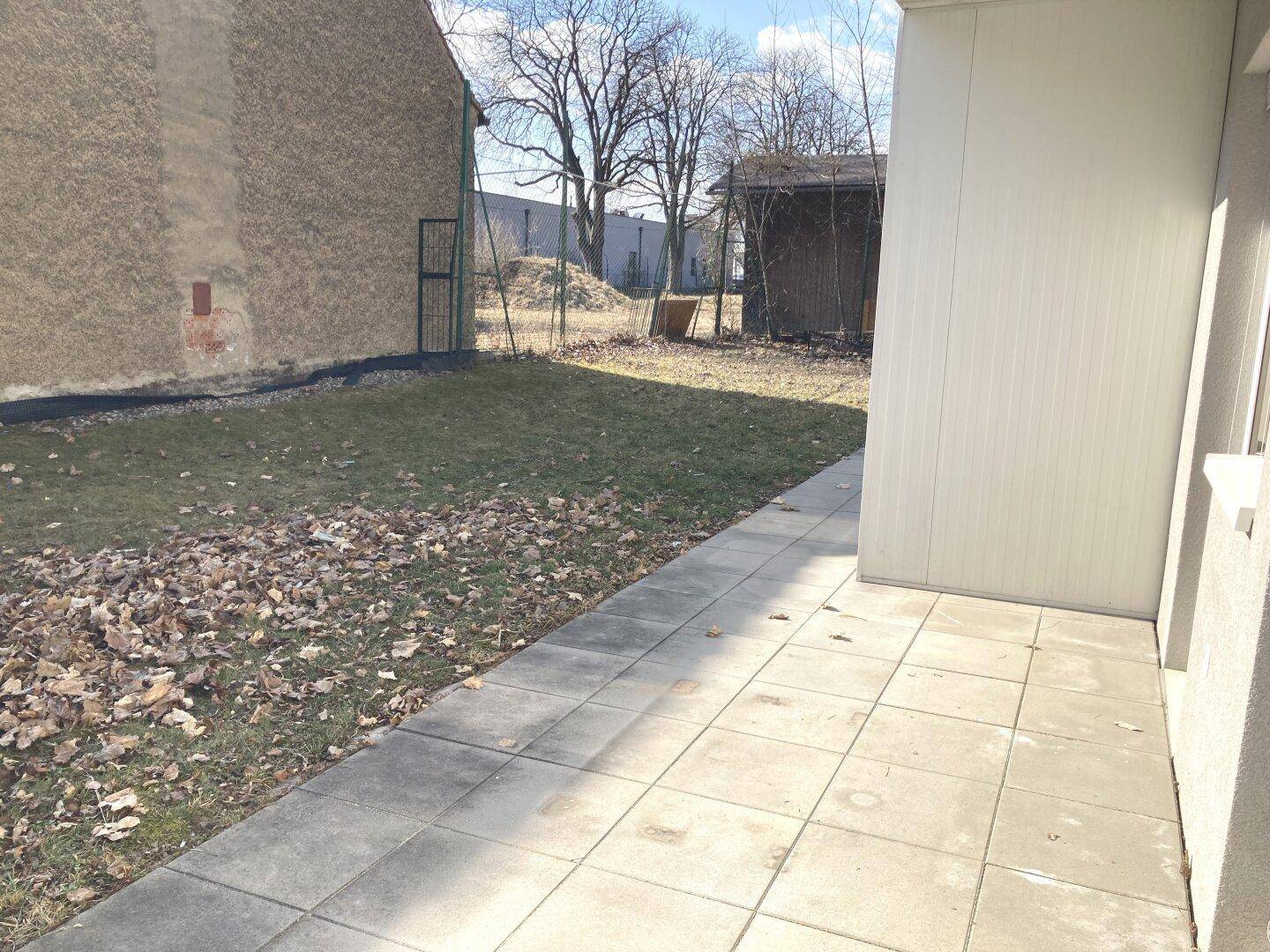 Kleiner Gartenbereich mit Rasenfläche und gepflastertem Weg neben der Terrasse.