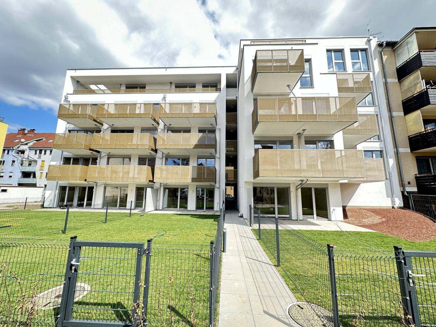 Neubau-Wohngebäude mit zeitgenössischer Architektur, hellen Balkonen und umzäuntem Vorgarten.