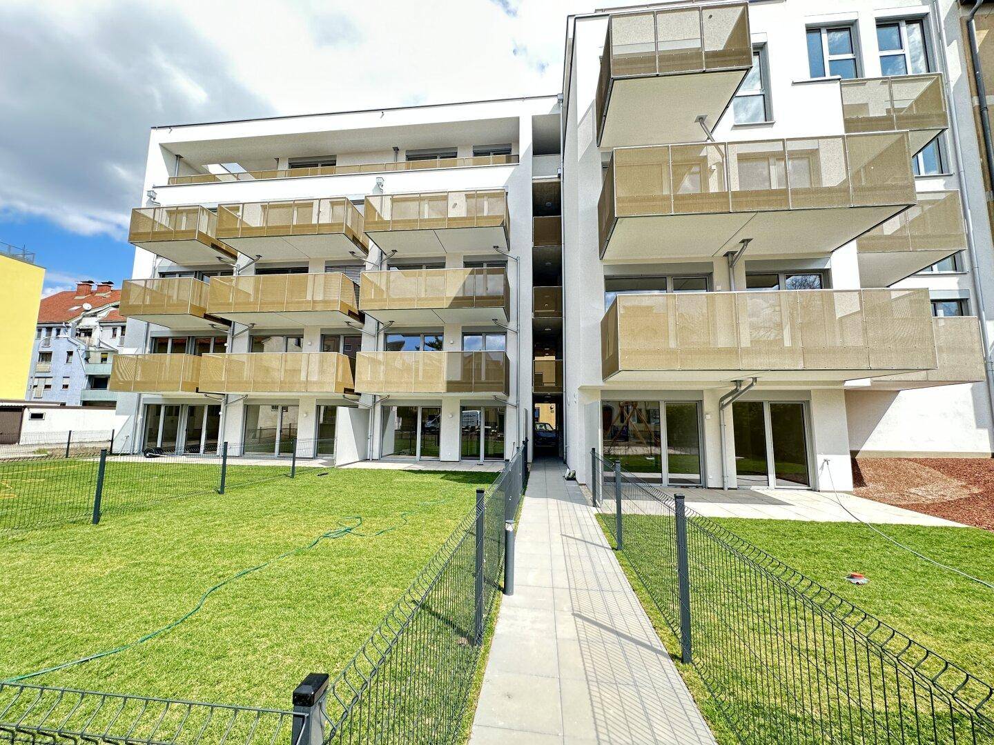 Weißes Wohnhaus im modernen Stil mit mehreren Balkonen und einer Rasenfläche im Vordergrund.