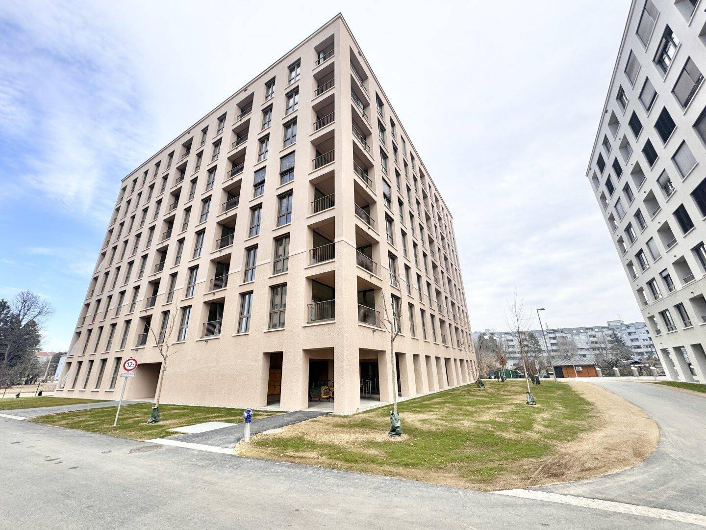Modernes Wohngebäude mit heller Fassade, Balkonen und umliegenden Grünflächen.