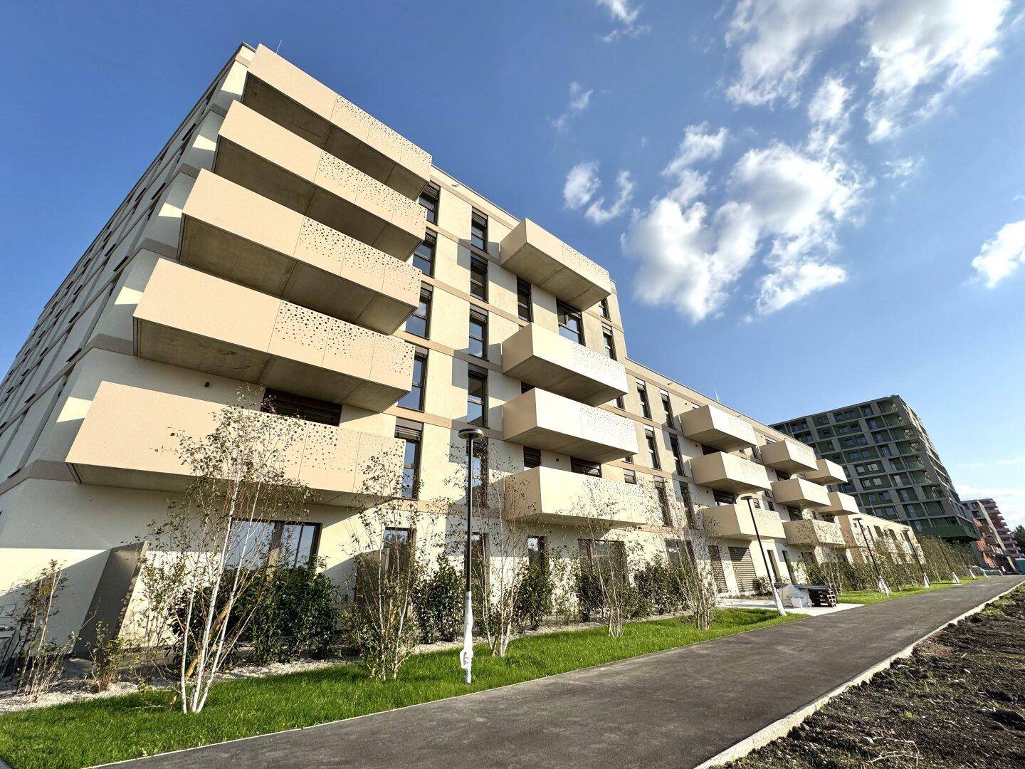 Moderne Wohngebäude mit zahlreichen Balkonen und gepflegten Grünanlagen unter blauem Himmel.