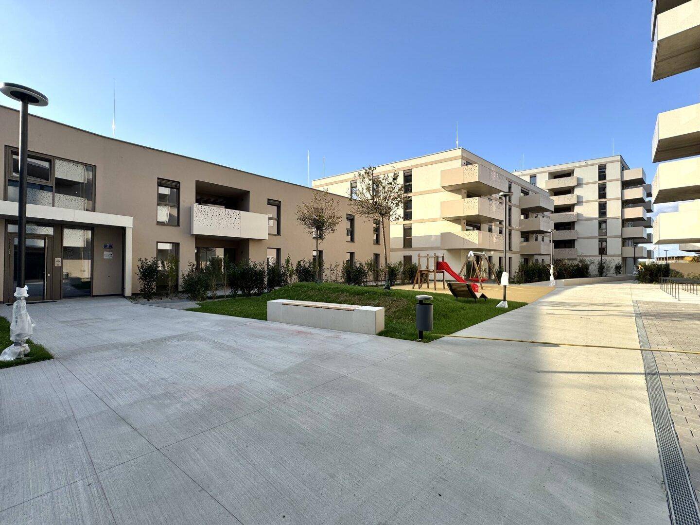 Außenansicht eines modernen Wohnkomplexes mit Grünflächen und Kinderspielplatz.