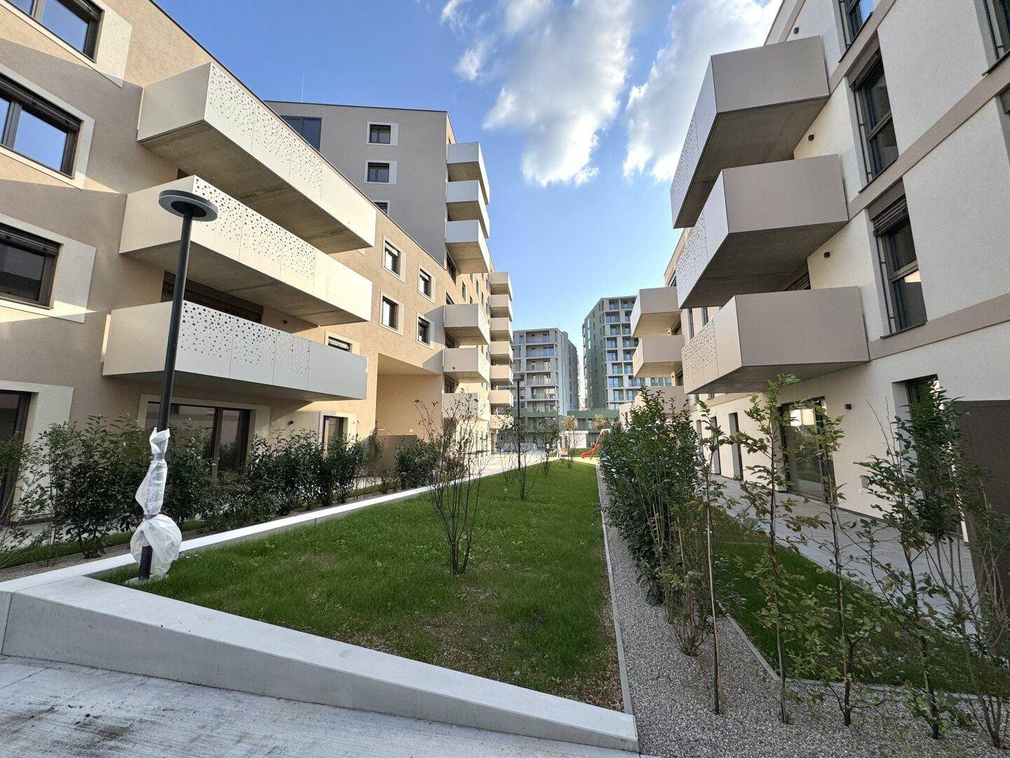Innenhof eines modernen Wohnkomplexes mit gepflegten Grünflächen und Wegen.