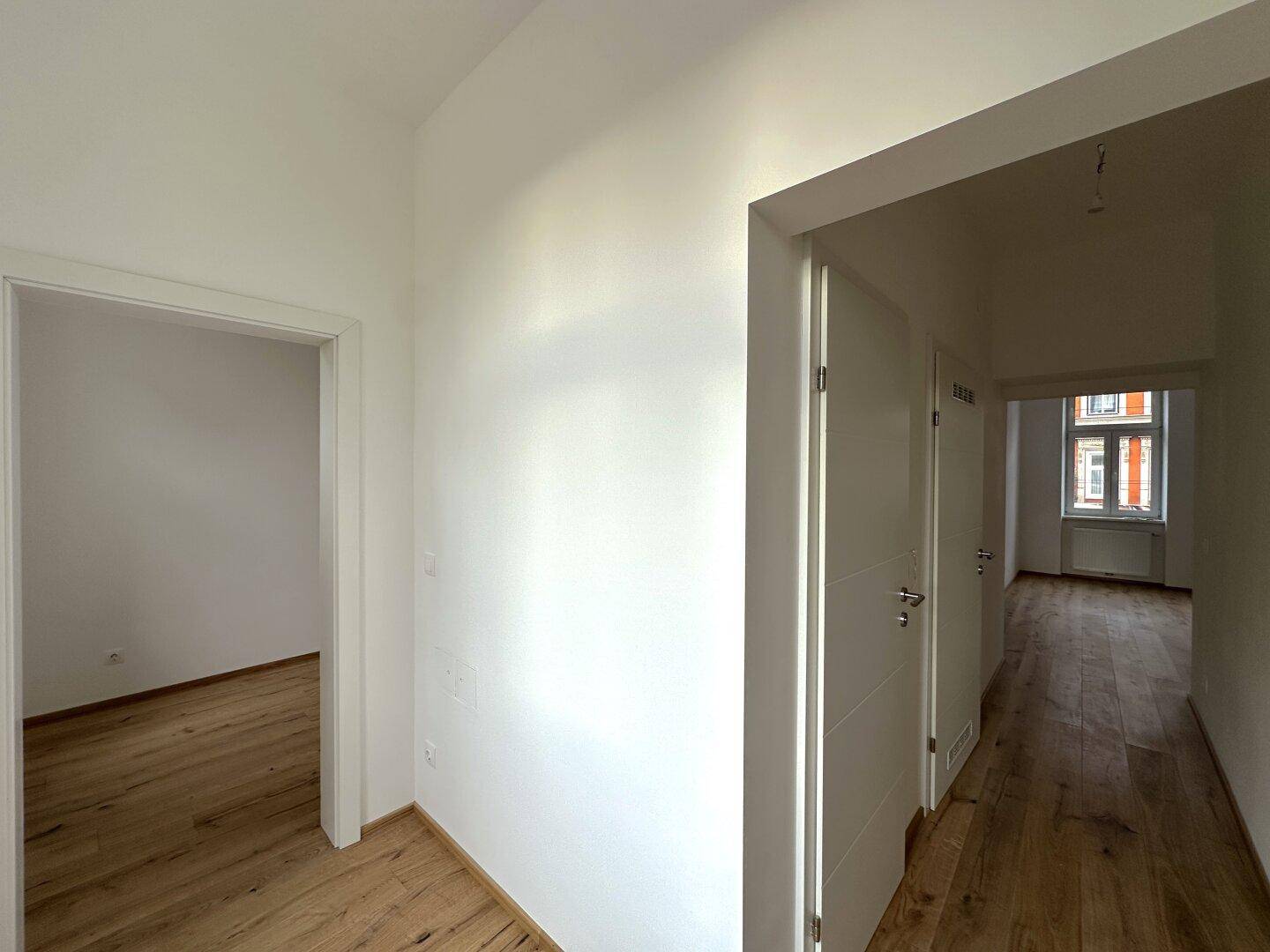 Heller Flur mit Holzboden und mehreren Türen, der einen Blick in angrenzende, leere Räume bietet.