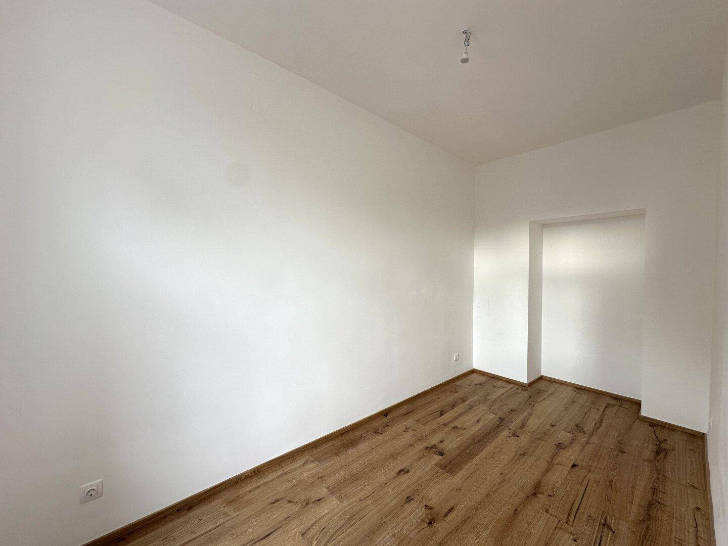 Leerer Raum mit warmem Holzboden und weißen Wänden, ideal für individuelle Einrichtungsideen.