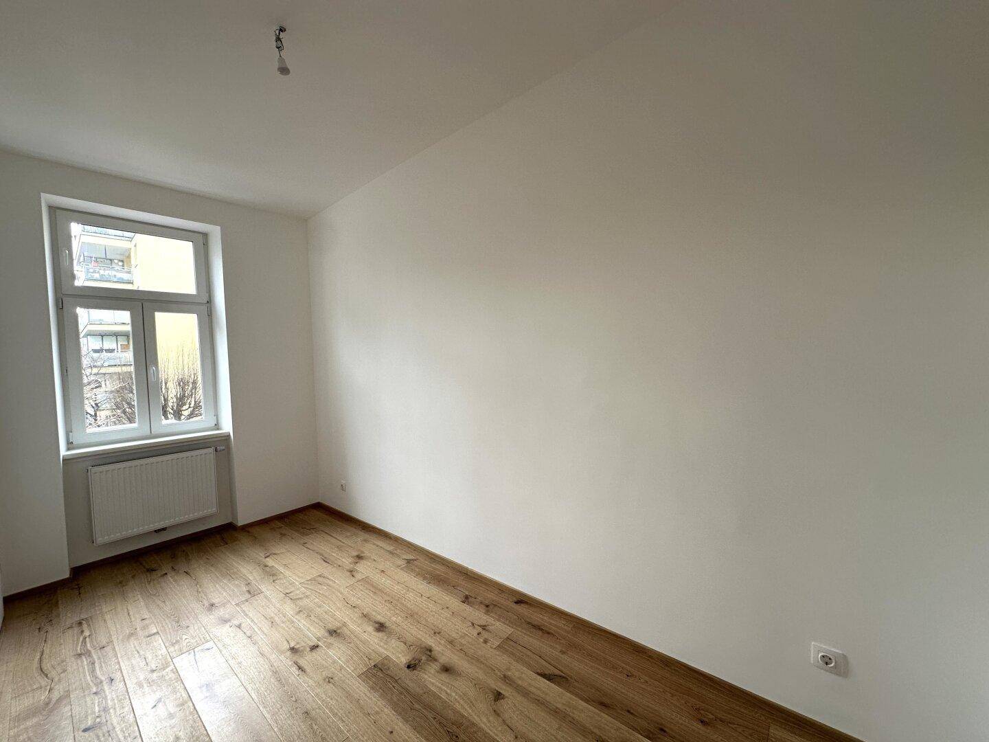 Geräumiges, leeres Zimmer mit Holzboden und einem Fenster, das eine angenehme Atmosphäre schafft.