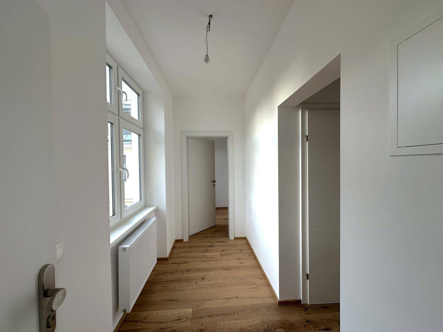 Langer, heller Flur mit Holzboden und Fenstern, die Tageslicht in den Eingangsbereich bringen.