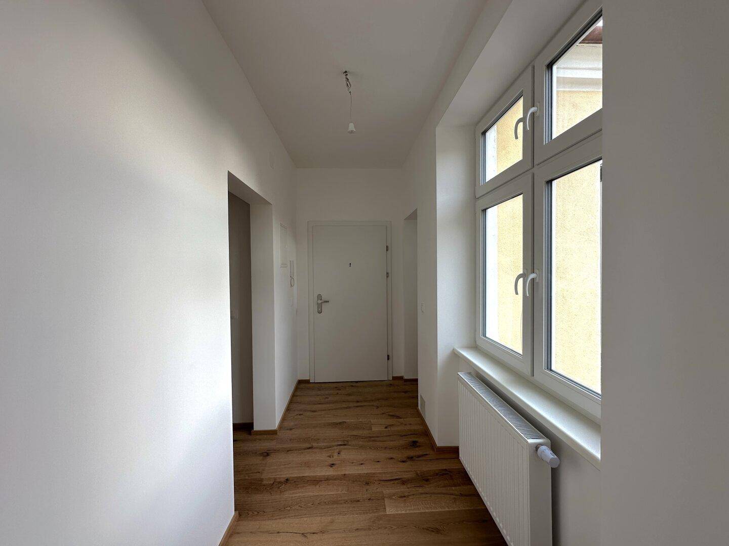 Heller Flur mit Holzboden und einem großen Fenster, das den Raum mit Tageslicht füllt.