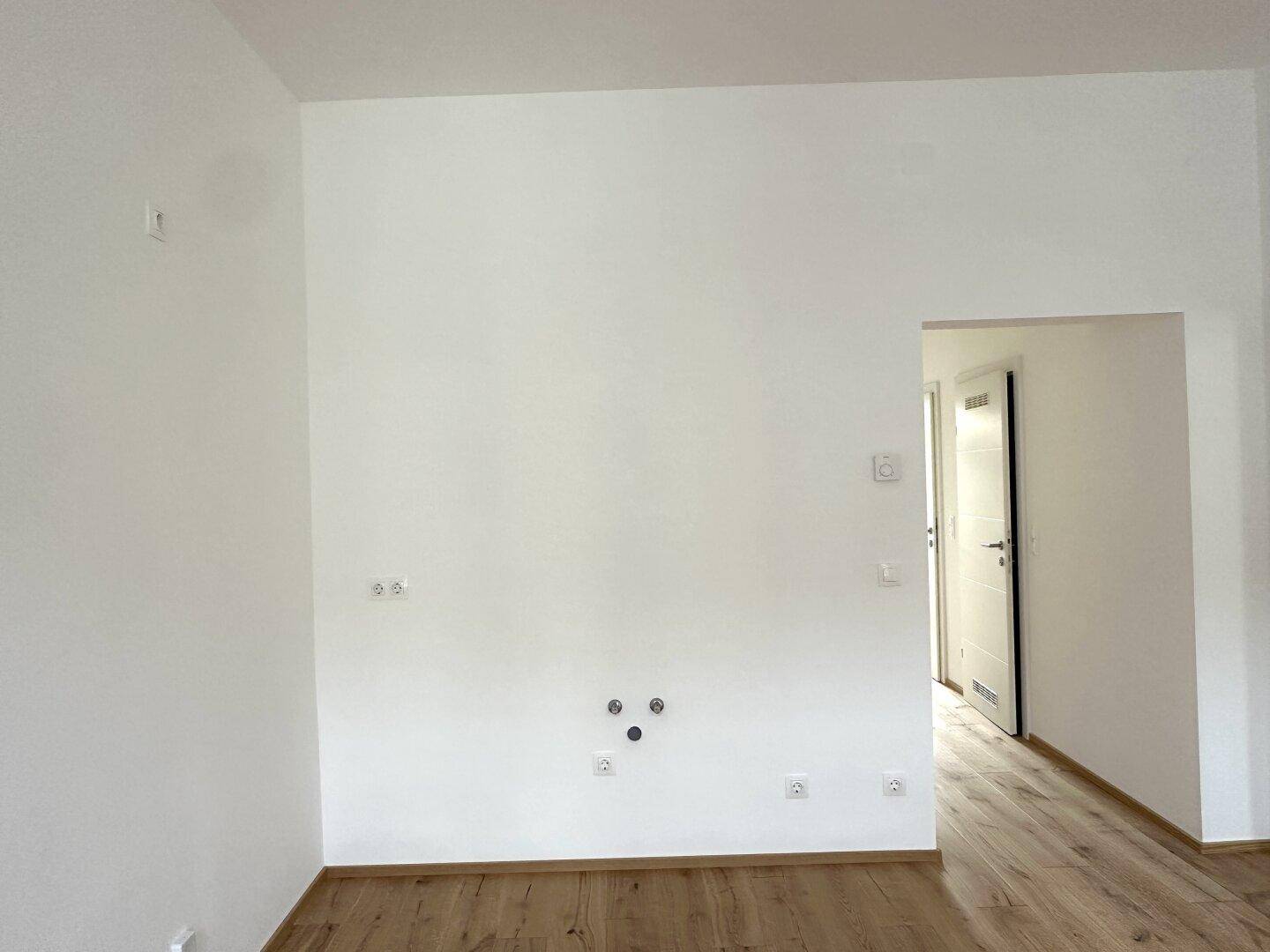 Heller Raum mit Holzboden und Anschlüssen für eine Küche, die auf ihre Einrichtung wartet.