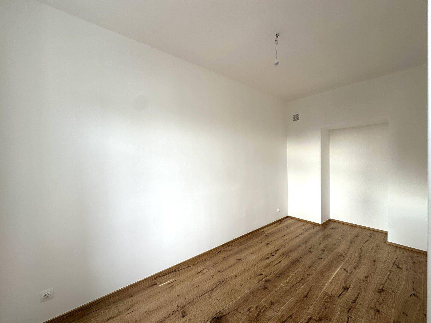 Leeres Zimmer mit Holzboden und weiß gestrichenen Wänden, bereit für die individuelle Gestaltung.
