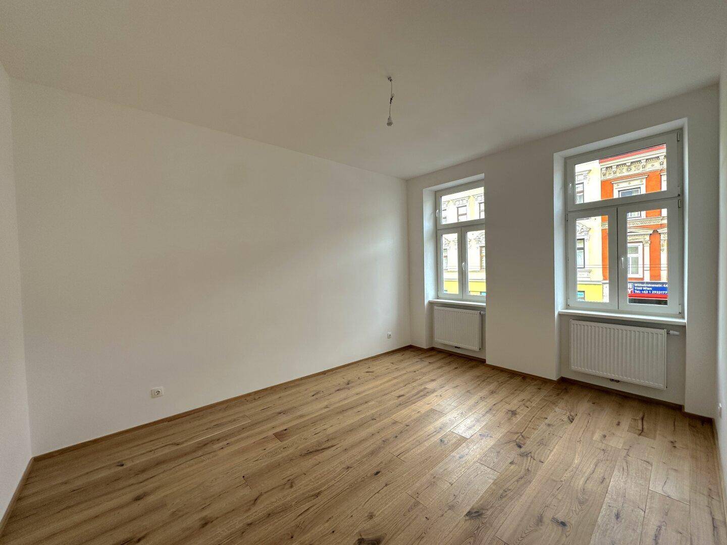 Lichtdurchfluteter Raum mit Holzboden und zwei Fenstern, ideal für einen Wohn- oder Essbereich.