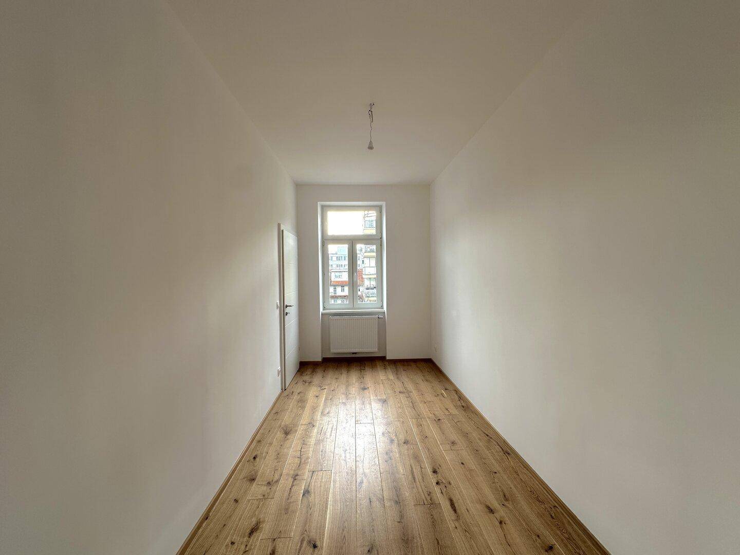 Helles Zimmer mit Holzboden und einem Fenster, das einen Blick auf die Umgebung bietet.