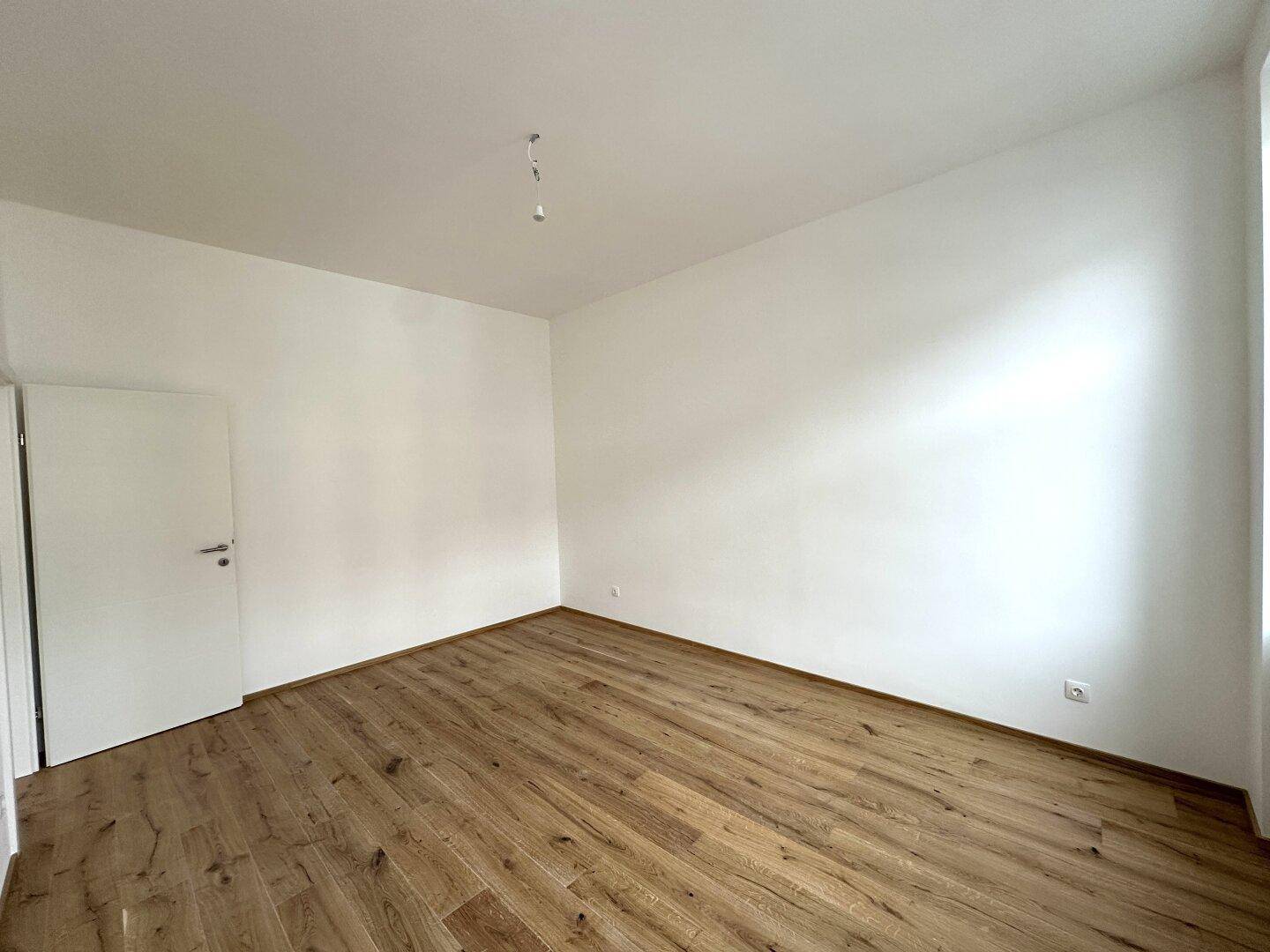 Leeres Zimmer mit Holzboden und weiß gestrichenen Wänden, bereit für neue Bewohner.