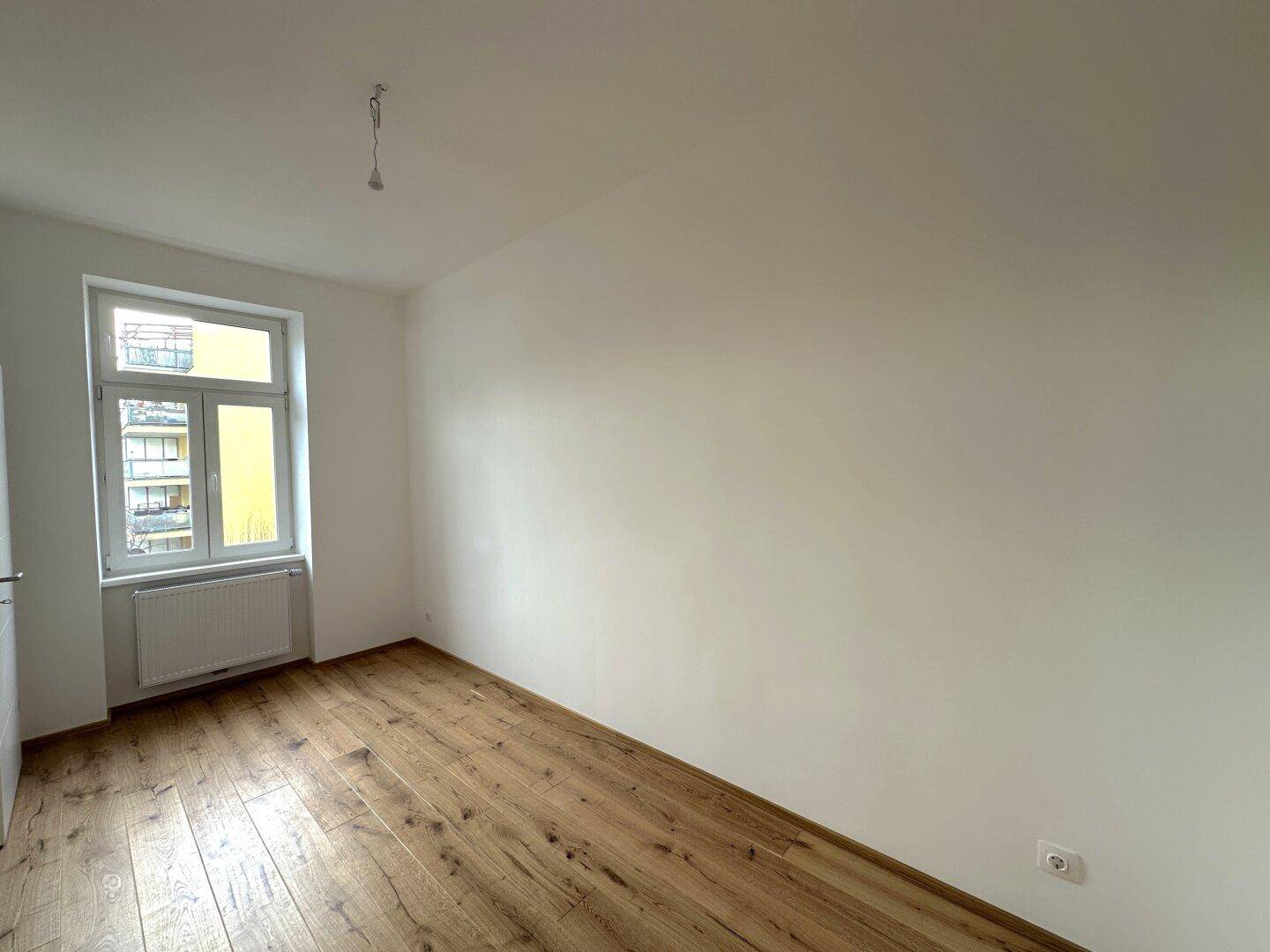 Geräumiges Zimmer mit Holzboden und weiß gestrichenen Wänden, ideal für Wohn- oder Schlafbereich.