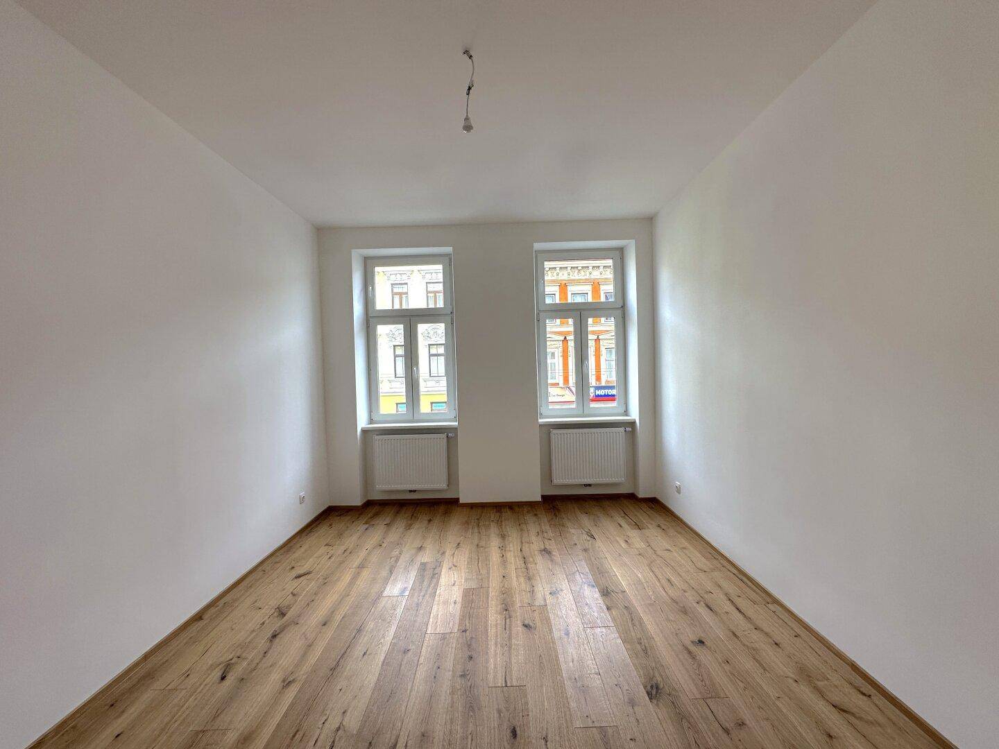 Heller, leerer Raum mit Holzboden und zwei Fenstern, die eine angenehme Wohnatmosphäre schaffen.