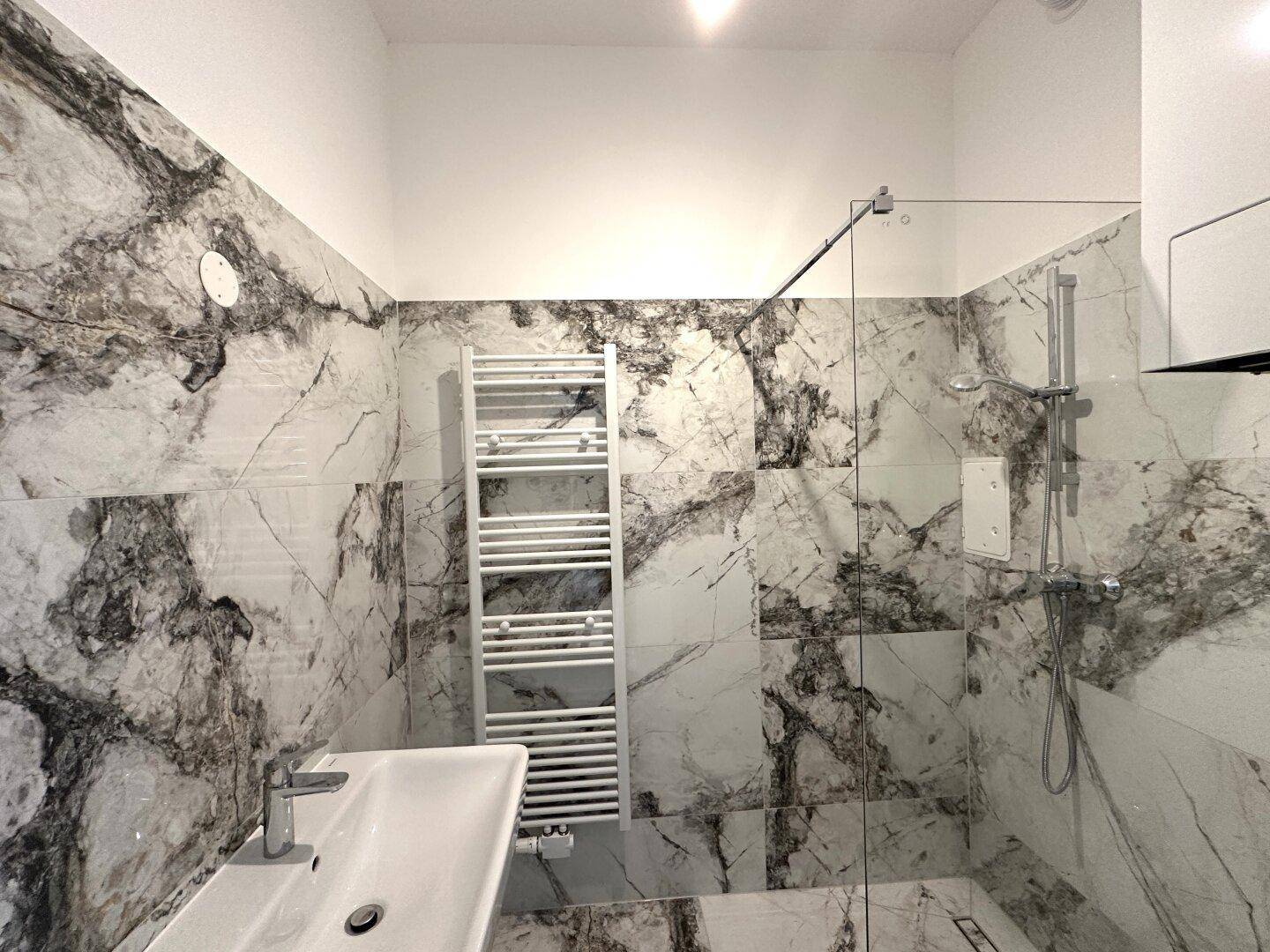 Modernes Badezimmer mit eleganten Marmorfliesen, begehbarer Dusche und beheiztem Handtuchhalter.