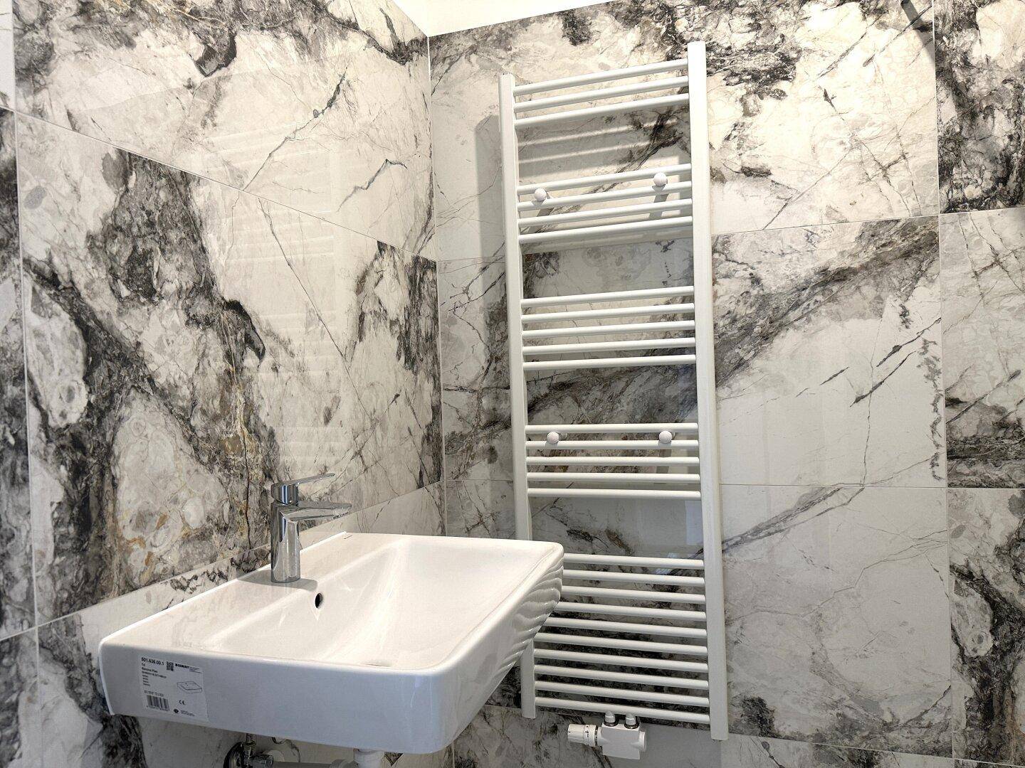 Detailansicht des modernen Waschbeckens und des beheizten Handtuchhalters im eleganten Badezimmer.
