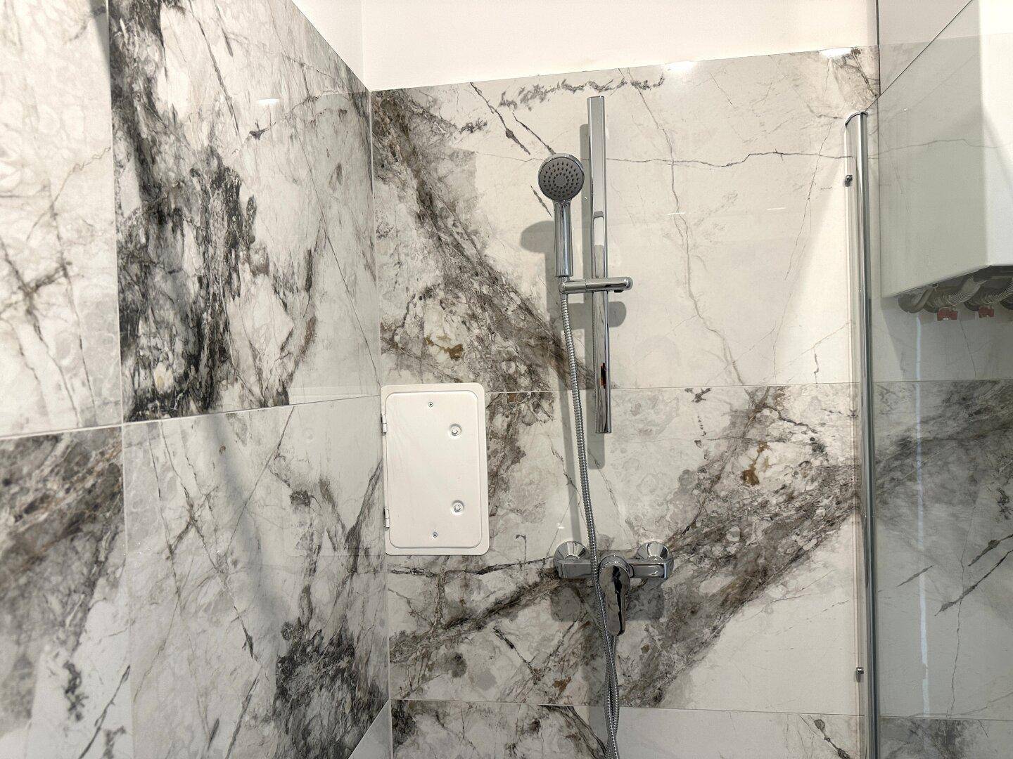 Duschbereich mit moderner Armatur und eleganten Marmorfliesen, die ein luxuriöses Ambiente schaffen.