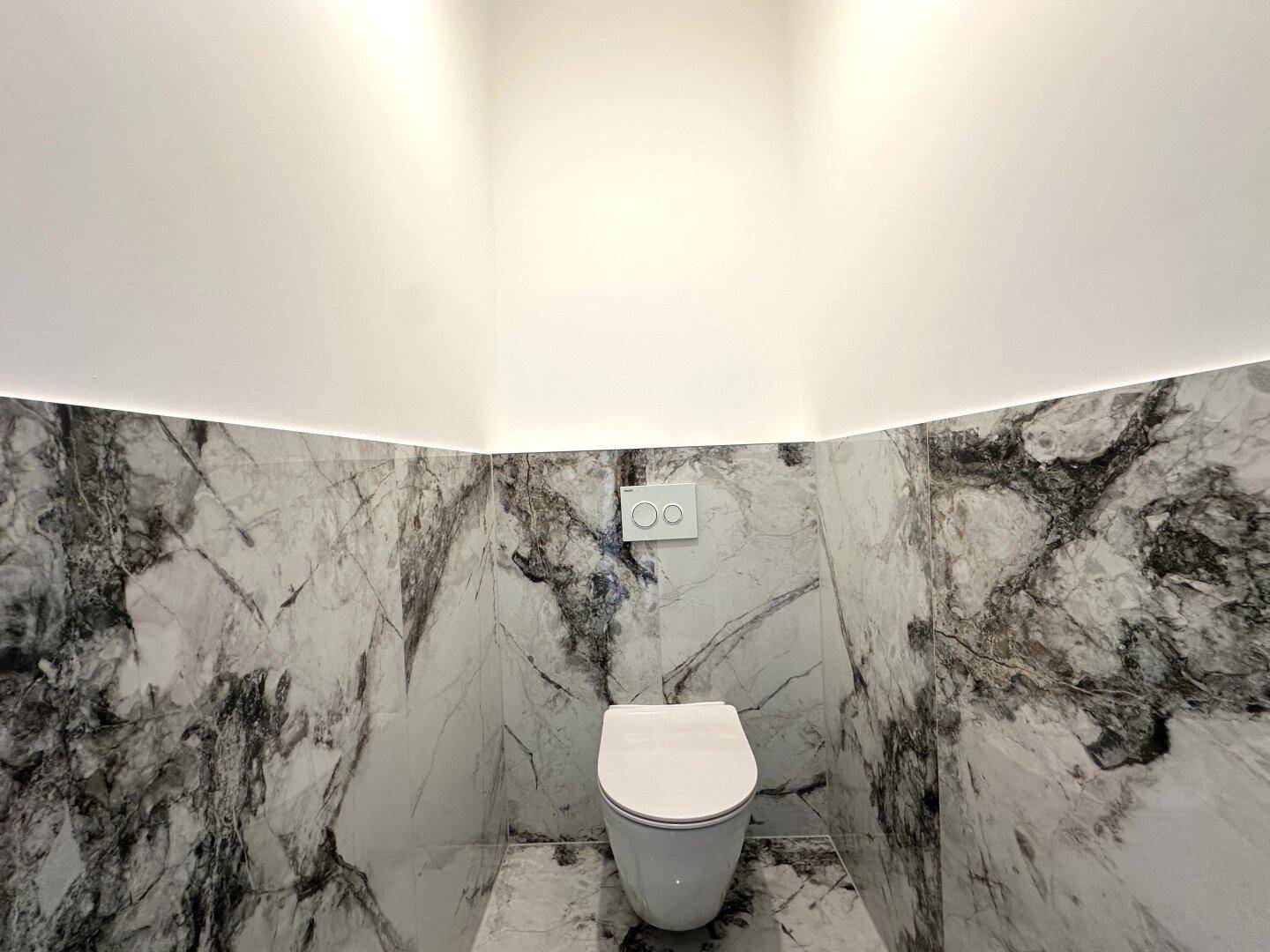 Modernes WC mit Wand-WC, Marmorfliesen und indirekter Beleuchtung für eine stilvolle Atmosphäre.