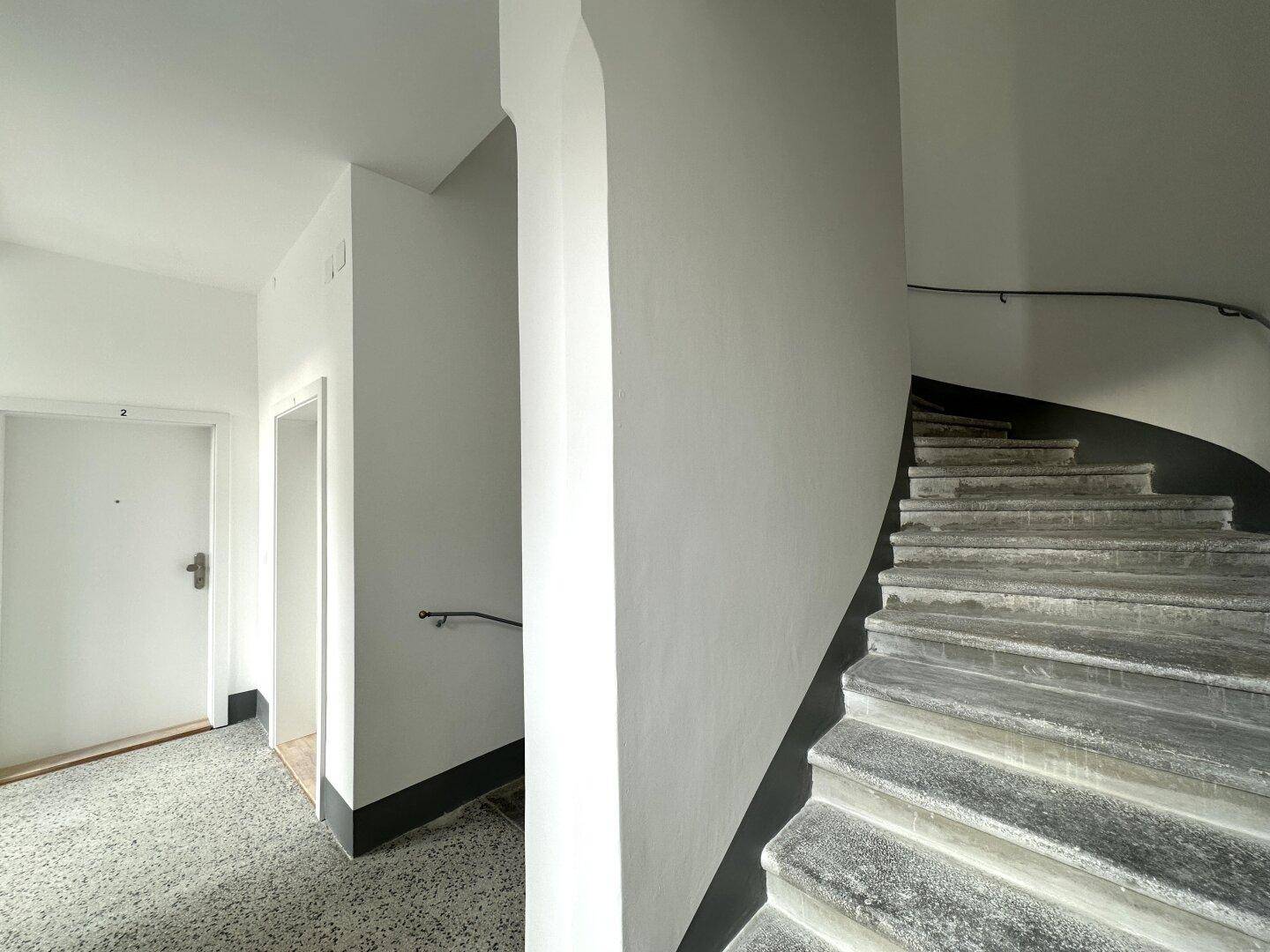 Eingangsbereich mit Steintreppe und Handlauf, der den Zugang zu den Wohneinheiten ermöglicht.