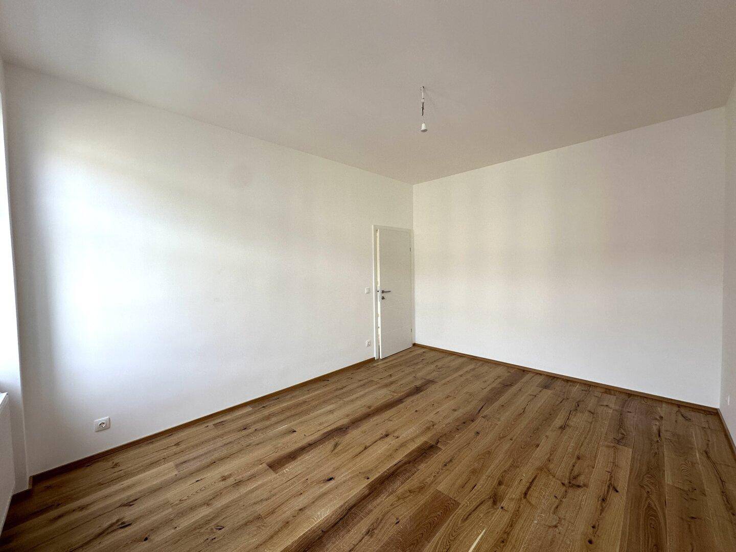 Leeres Zimmer mit Holzboden und weiß gestrichenen Wänden, bereit für die individuelle Einrichtung.