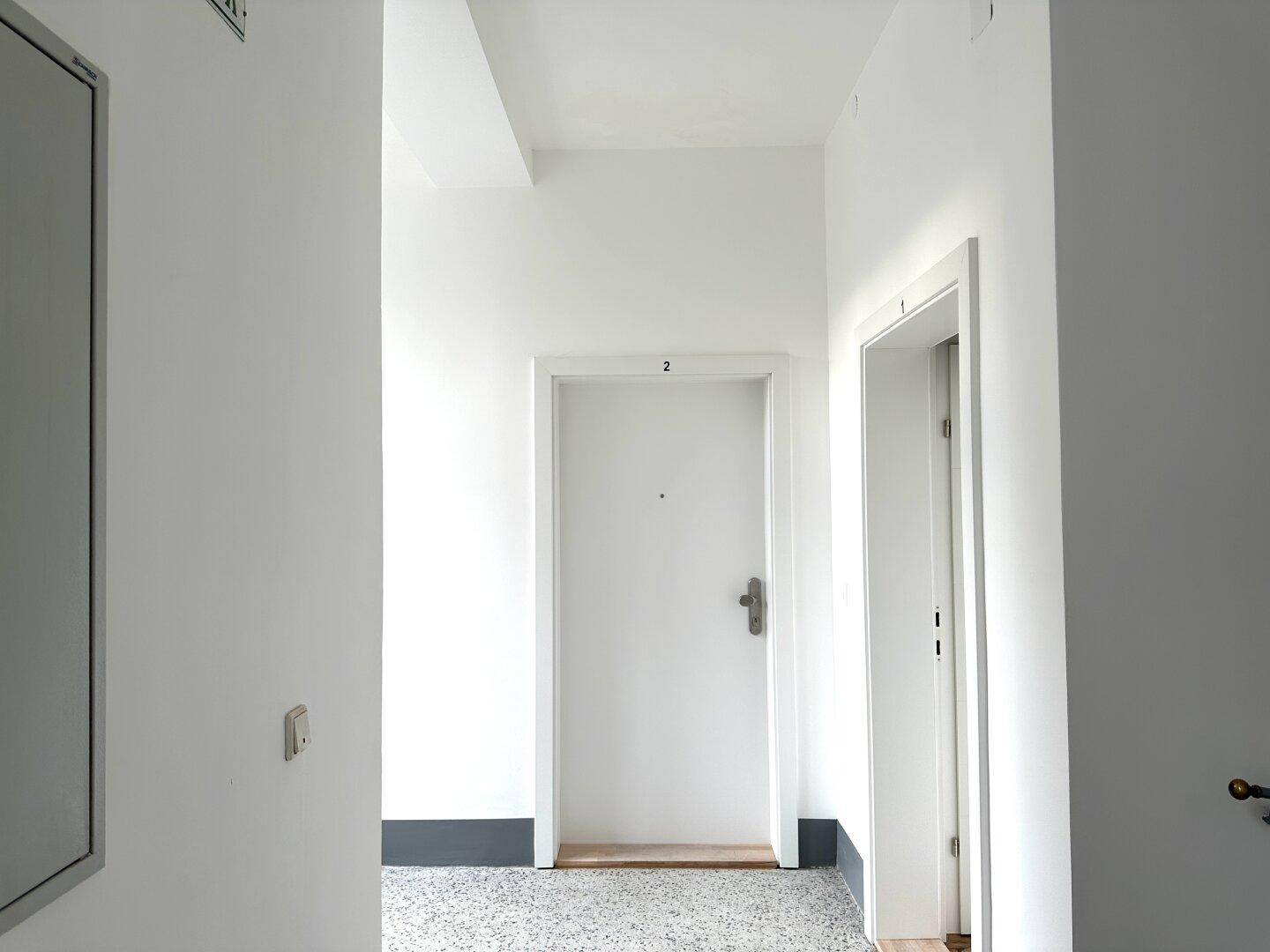 Heller Gemeinschaftsflur mit Wohnungstür Nummer zwei und einem Spiegel an der Wand.