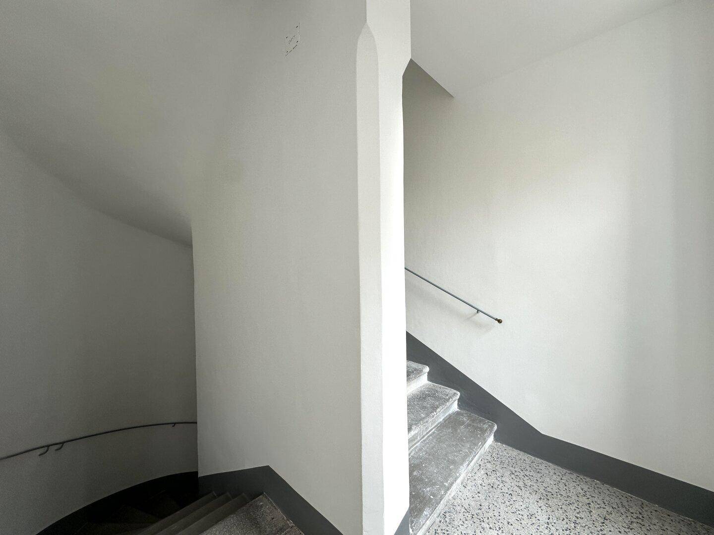 Wendeltreppe mit Steinstufen und schlichtem Handlauf in einem gepflegten Treppenhaus.