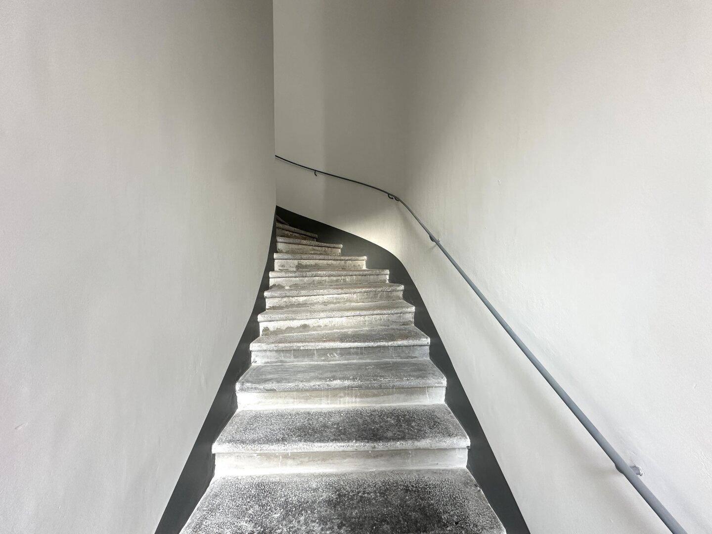 Wendeltreppe mit schlichtem Geländer und hellen Wänden in einem Treppenhaus.