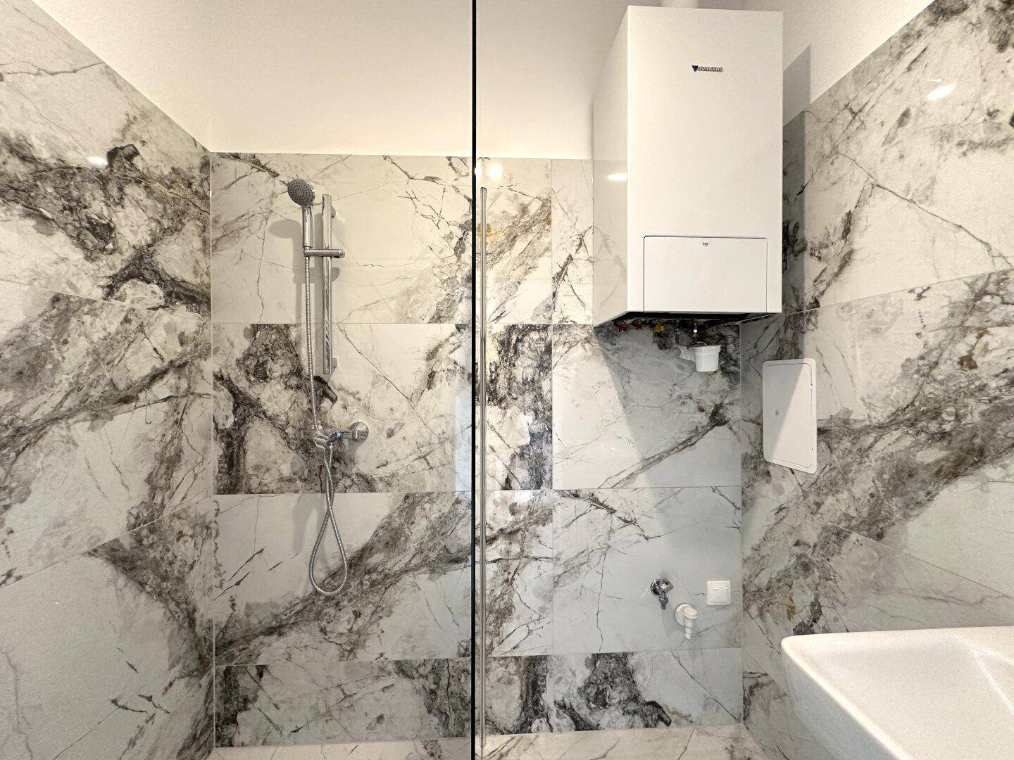 Elegantes Badezimmer mit Marmorfliesen, einer geräumigen Duschkabine und einem Wandheizkessel.