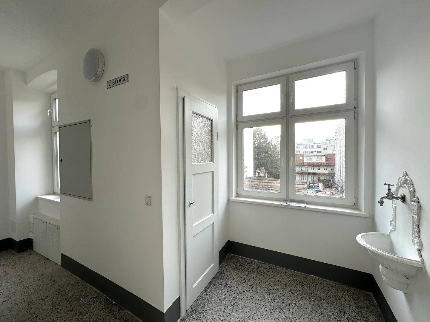 Heller Flur mit Fenster, kleinem Waschbecken und Blick auf die Umgebung.