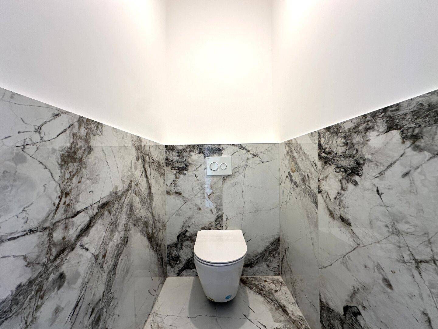 Separate Toilette mit modernen Marmorfliesen und einer wandmontierten Toilette.