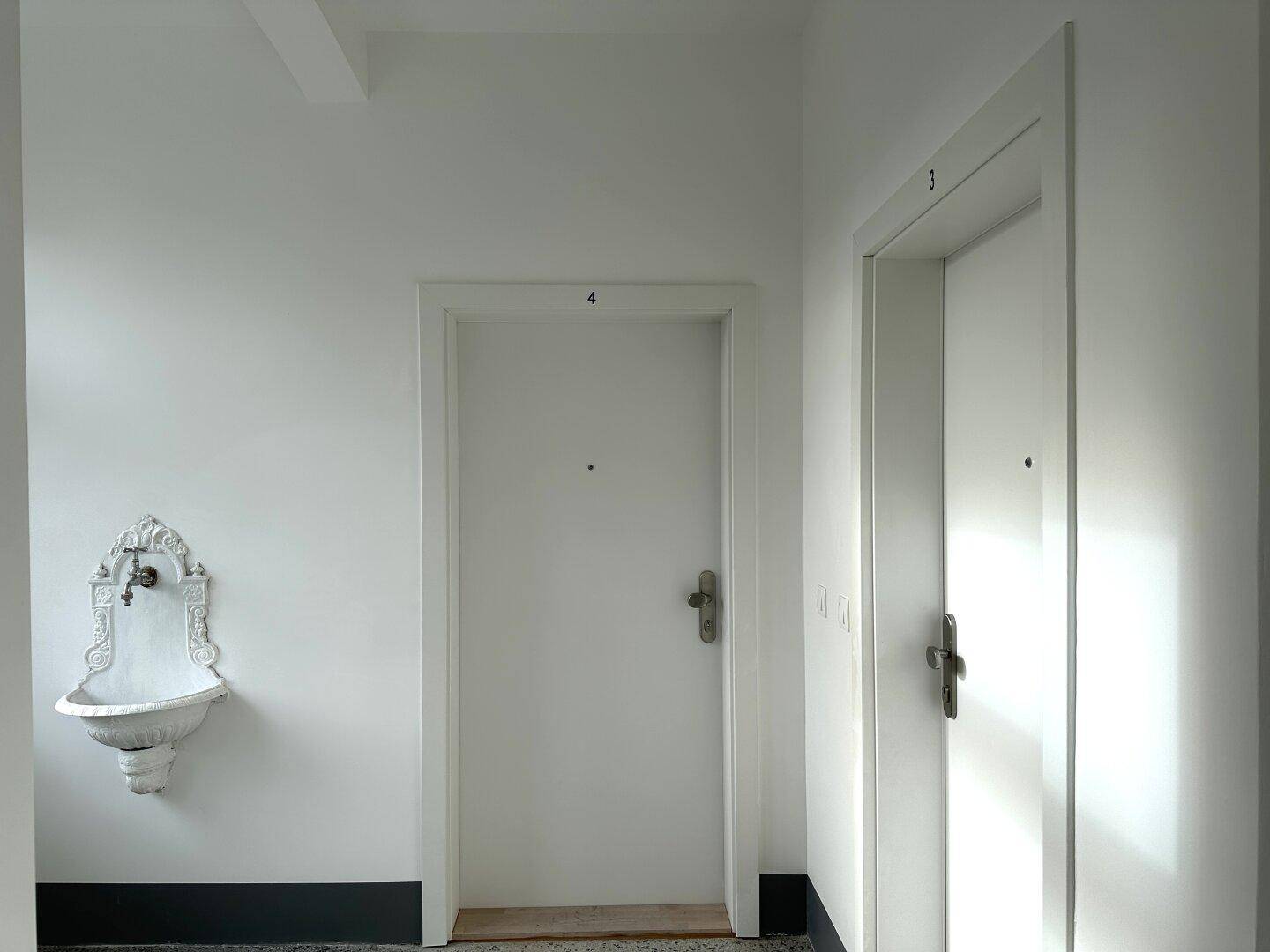 Flur mit zwei Wohnungstüren und einem dekorativen Wandbrunnen, der einen klassischen Charme verleiht.
