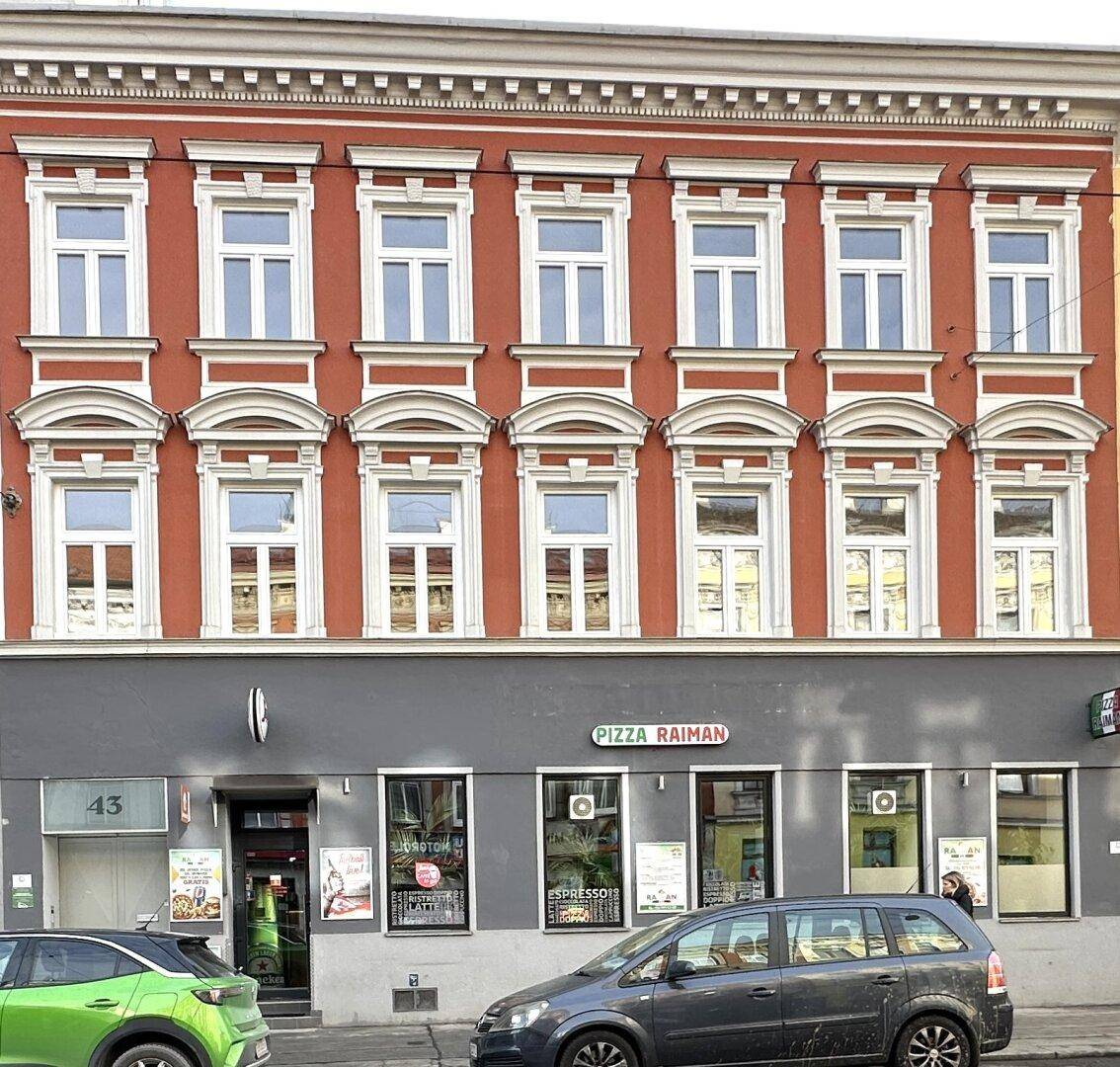 Historische rote Fassade eines Gebäudes mit vielen Fenstern und einem Geschäft im Erdgeschoss.