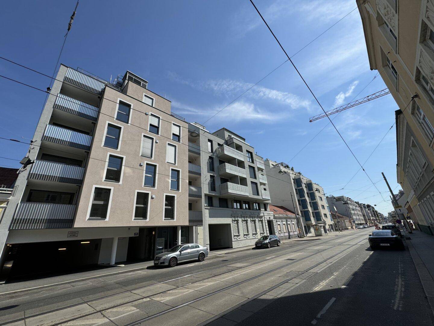 Lange Straßenansicht mit einem modernen Wohngebäude und Straßenbahnschienen im Vordergrund.