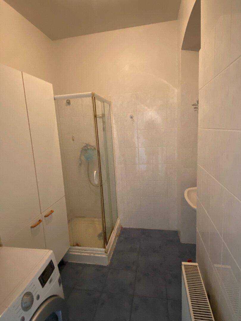 Funktionales Badezimmer mit Duschkabine, Waschbecken, Waschmaschine und weißen Fliesen.
