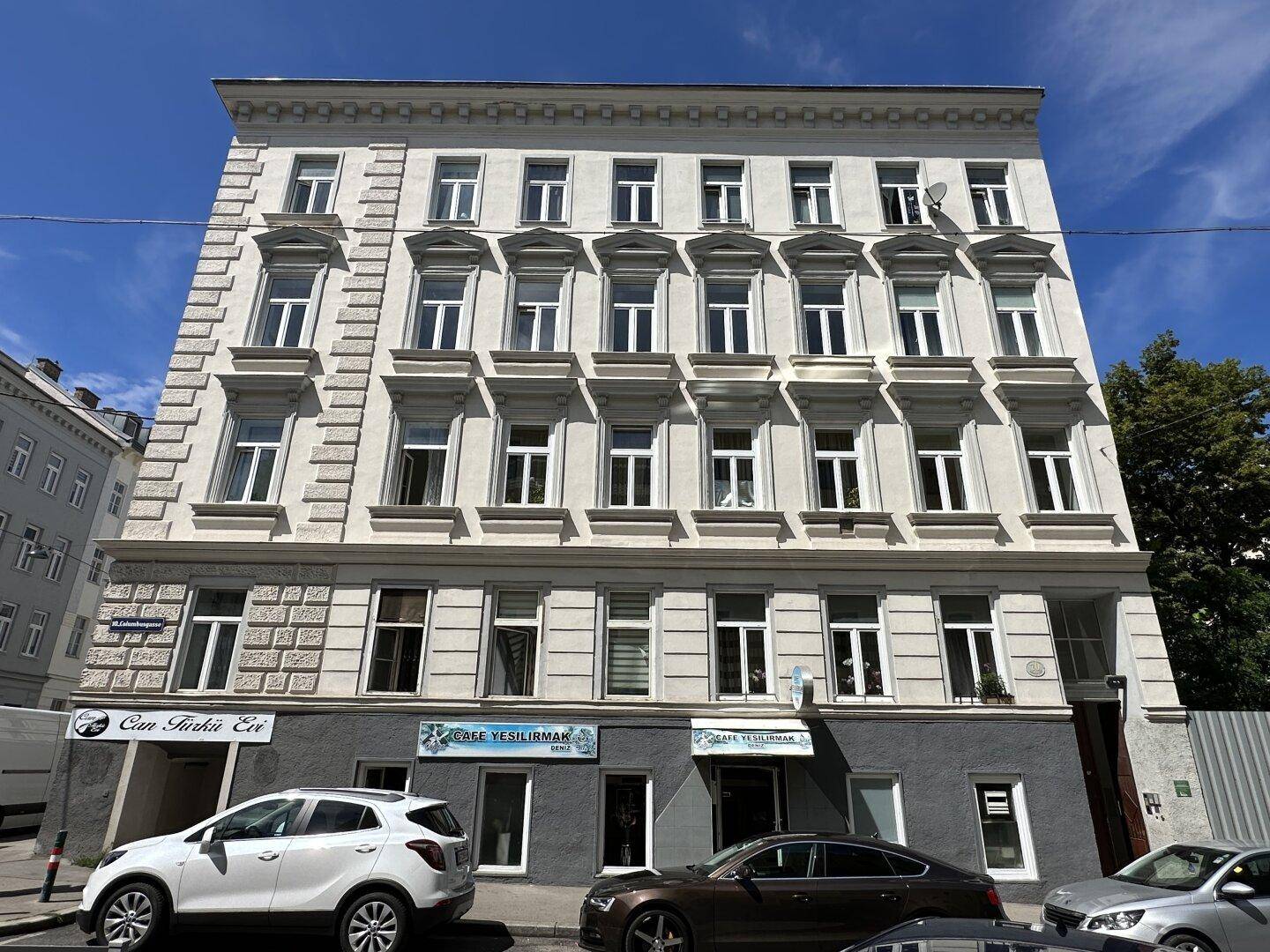 Historisches Mehrfamilienhaus mit vielen Fenstern und Geschäften im Erdgeschoss an einer Straße.