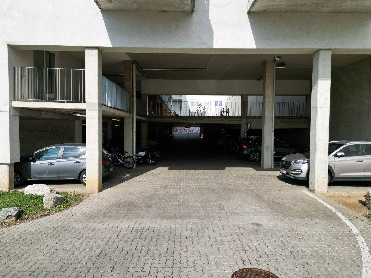 Überdachter Parkbereich unter dem Gebäude mit Stellplätzen für Fahrzeuge.