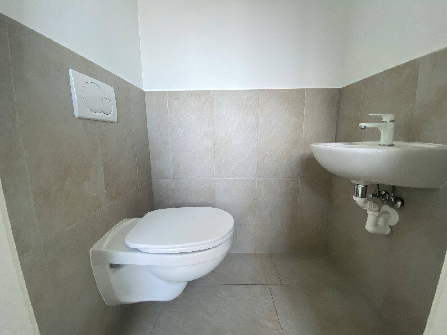 Funktionale Gästetoilette mit wandhängendem WC und kleinem Waschbecken, hell gefliest.