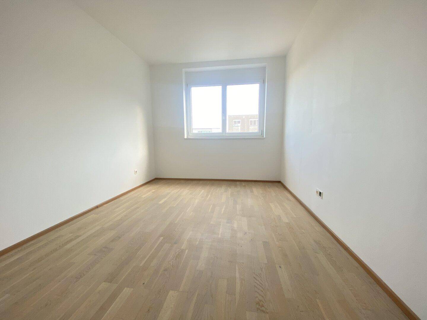 Freundliches Zimmer mit Parkettboden und großem Fenster, ideal als Schlaf- oder Arbeitszimmer.