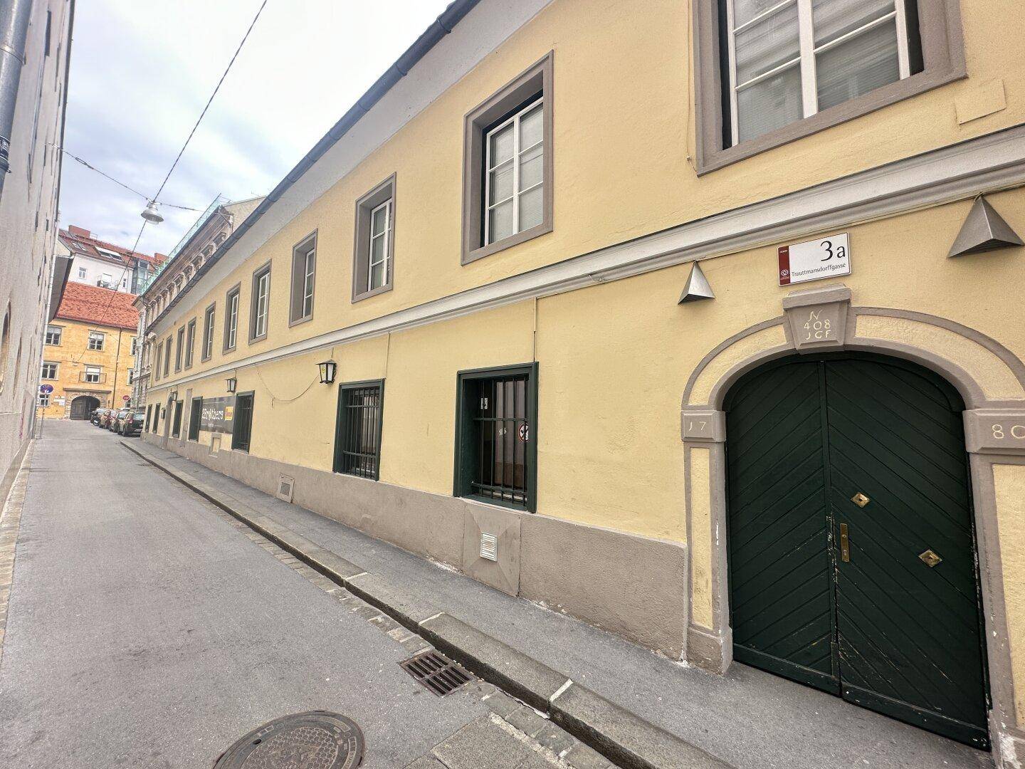 Historisches Gebäude mit gelber Fassade und grünen Türen in einer engen Gasse.