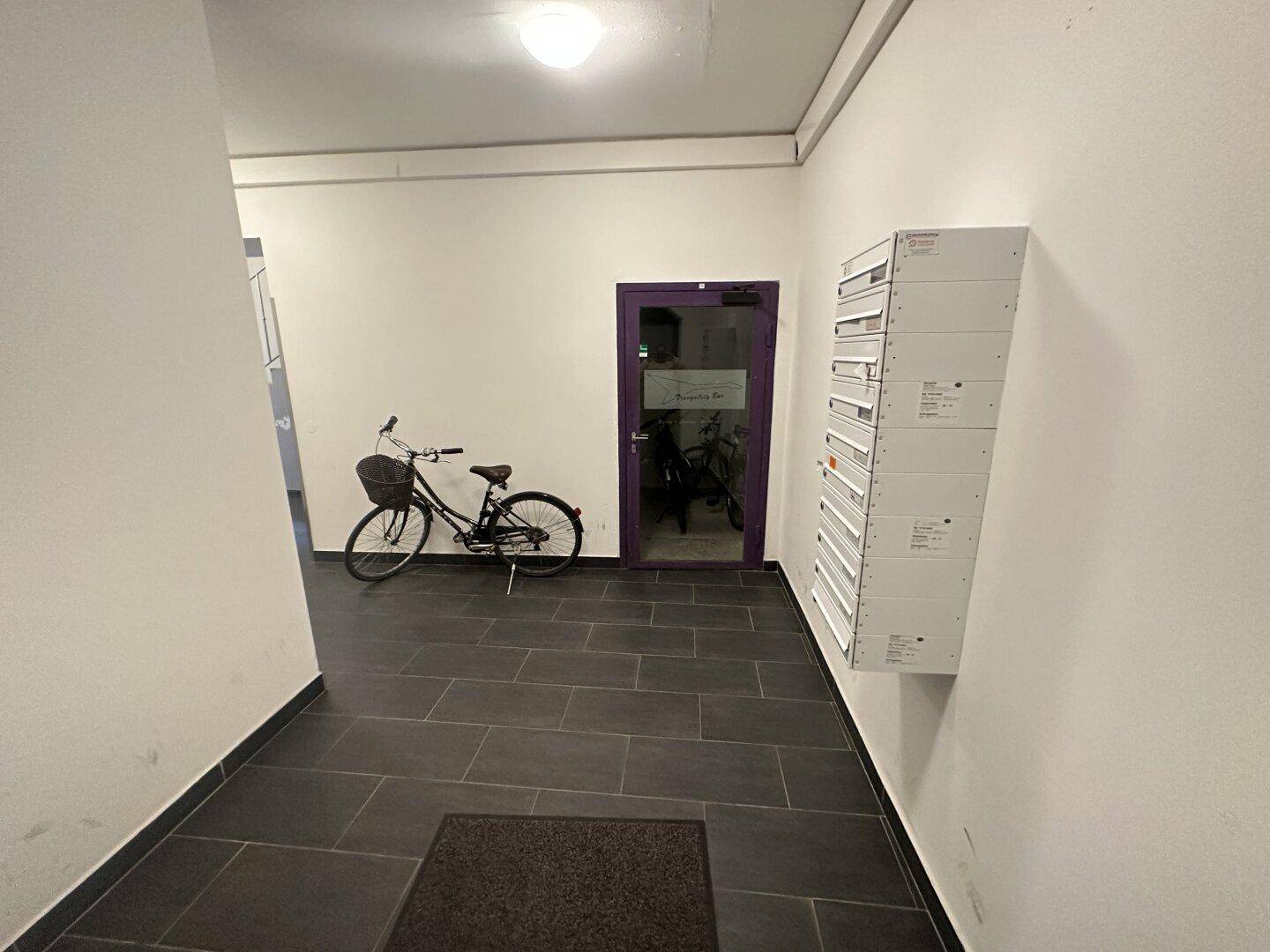 Eingangsbereich mit dunklem Fliesenboden, Briefkästen und Abstellmöglichkeit für Fahrräder.