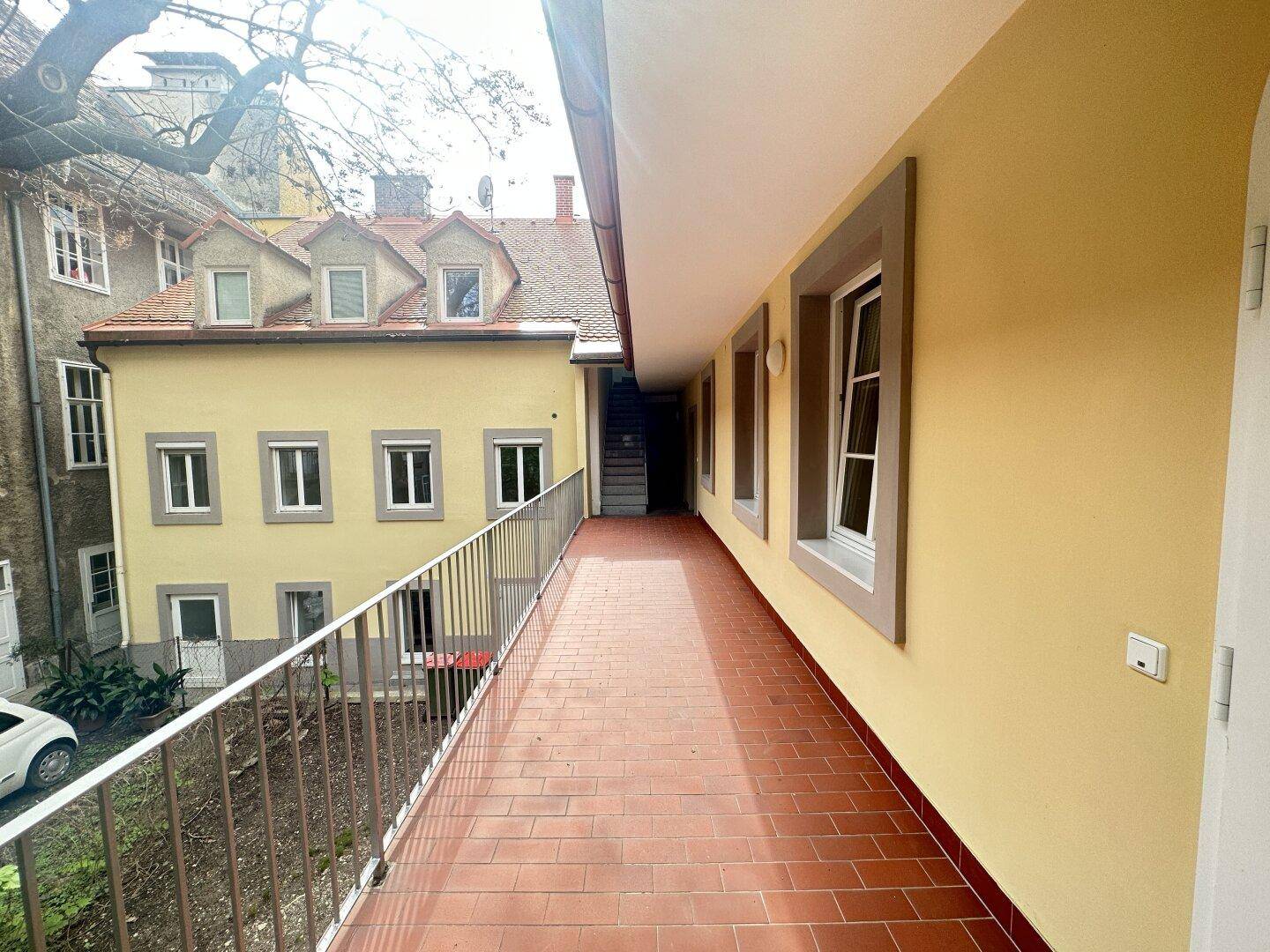 Langer Außenbalkon mit Terrakottafliesen und Blick auf den Innenhof des Gebäudes.