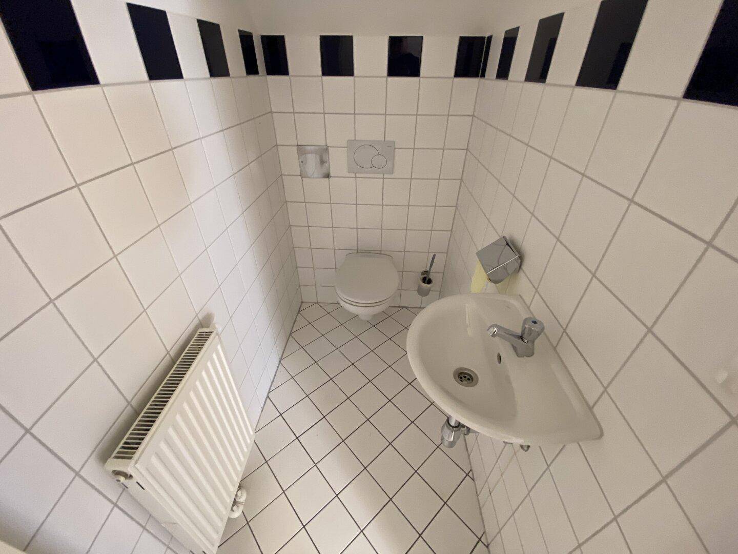 Kleines Gäste-WC mit weißen Fliesen, Wand-WC und einem Eckwaschbecken, funktional und sauber.