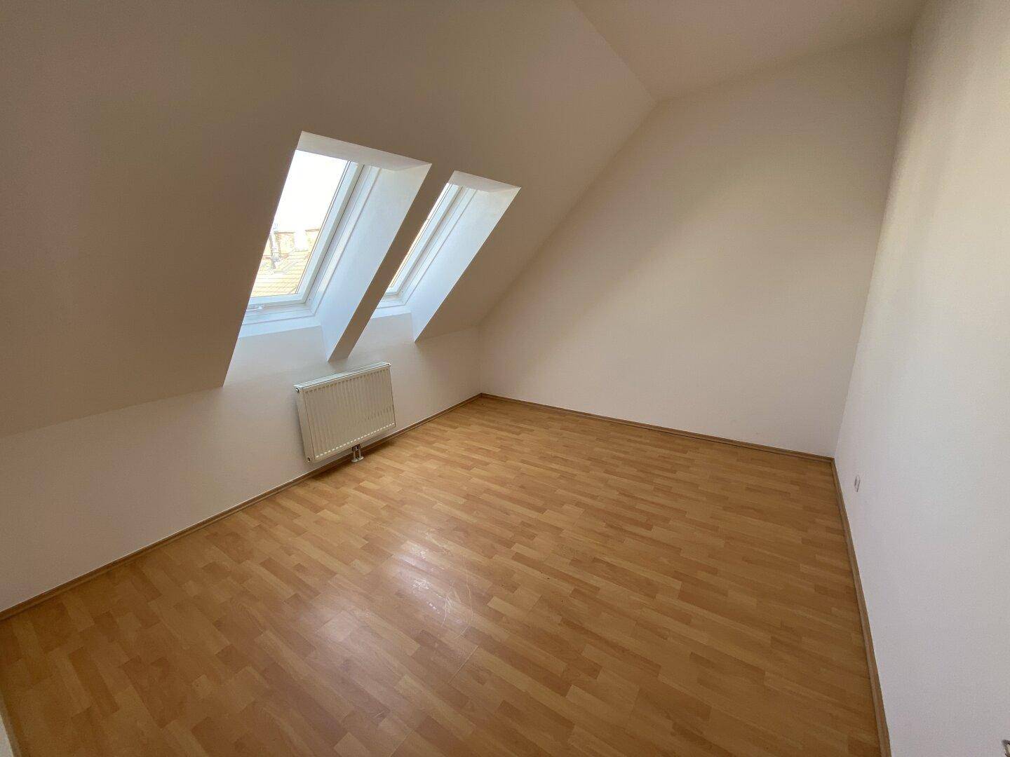 Gemütliches Schlafzimmer im Dachgeschoss mit schrägen Wänden, Holzfußboden und zwei Dachfenstern.