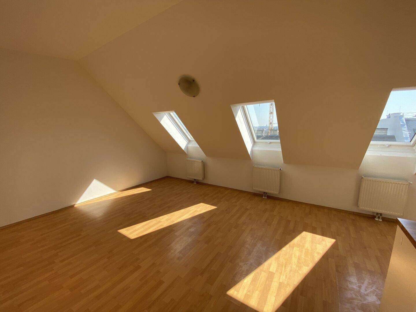 Geräumiger Dachgeschossraum mit schrägen Wänden, Holzfußboden und mehreren Dachfenstern für viel Tageslicht.