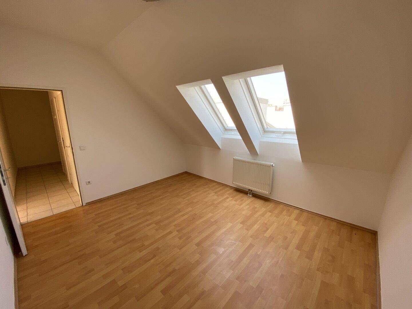 Helles Dachgeschosszimmer mit Holzfußboden, schrägen Wänden und zwei Dachfenstern, die den Raum erhellen.