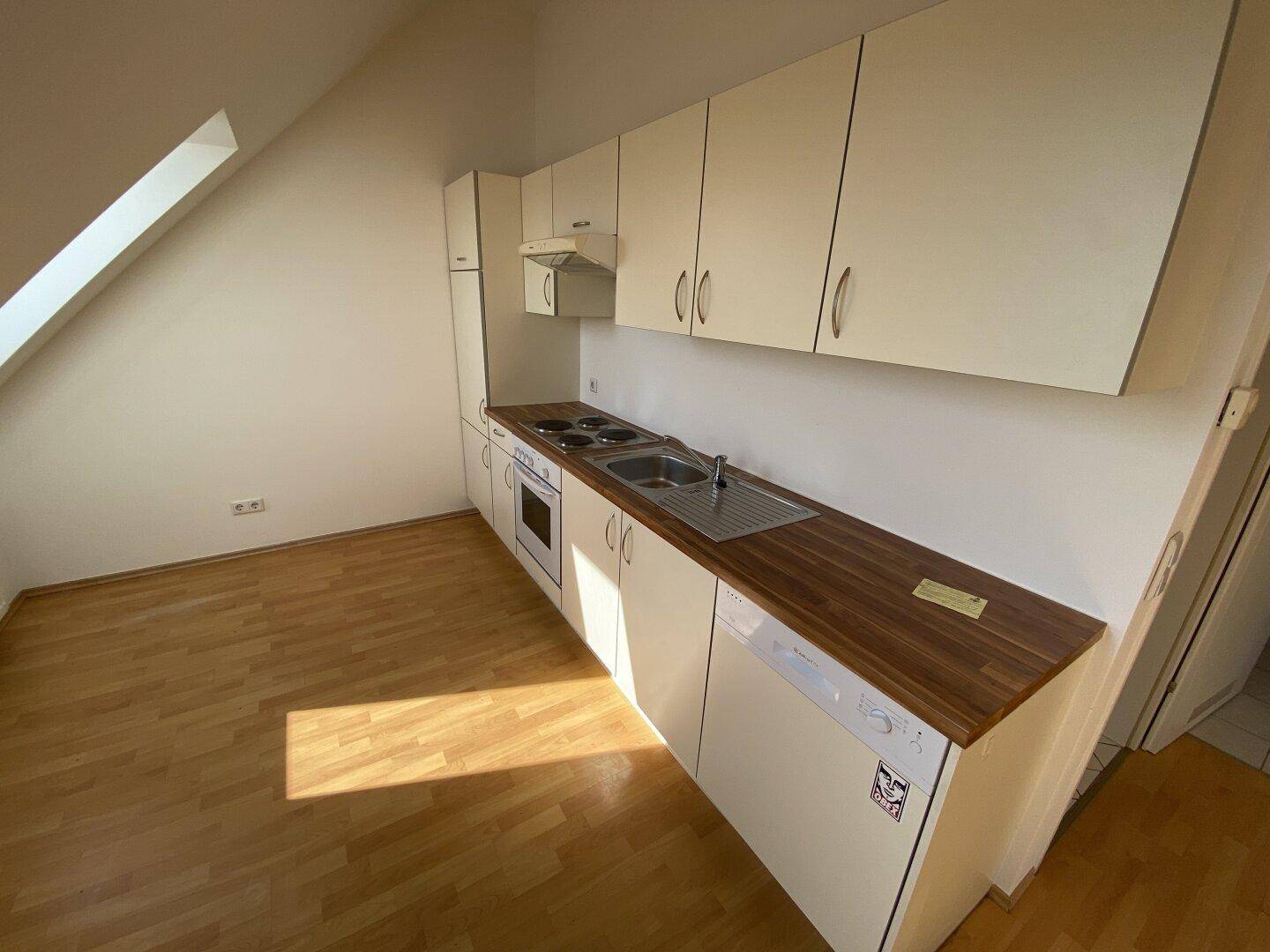 Funktionale Einbauküche mit weißen Schränken, Holzarbeitsplatte und einem Dachfenster für Tageslicht.
