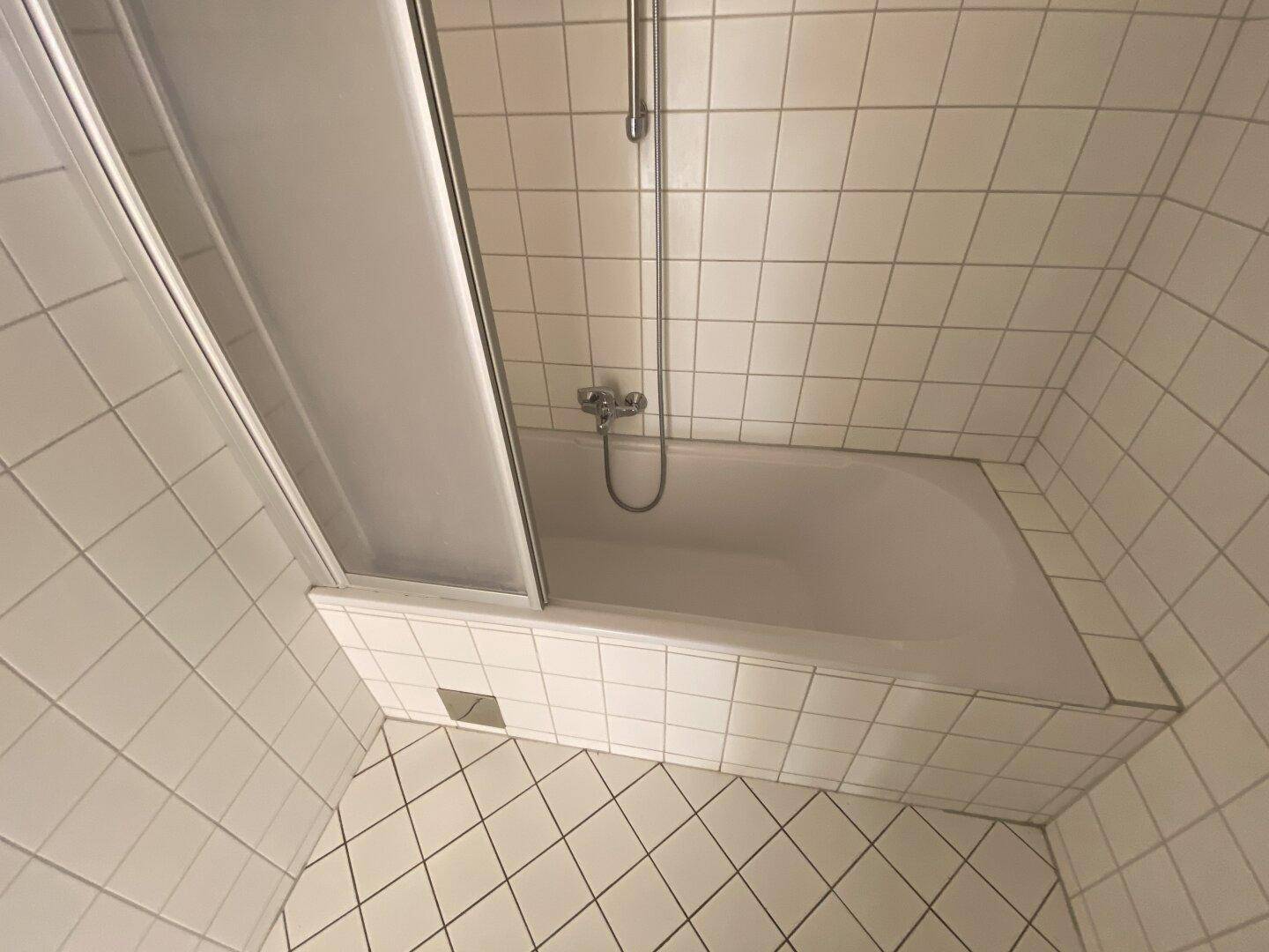 Badezimmer mit Badewanne und Duschabtrennung, komplett gefliest in Weiß, sauber und funktional.