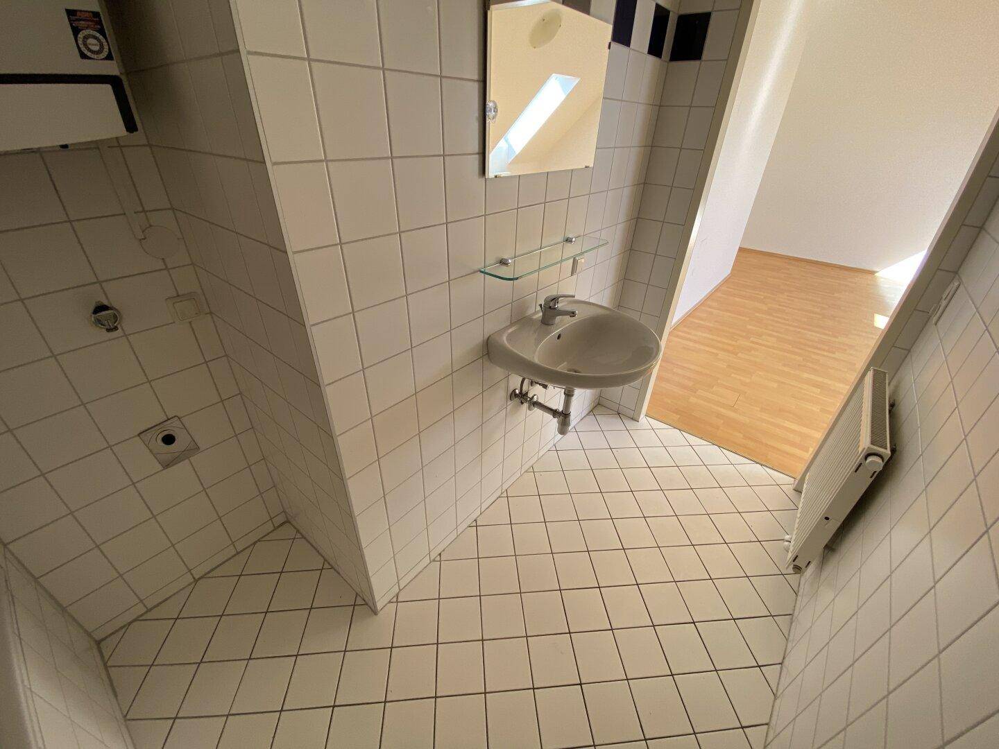 Badezimmer mit Waschbecken, Spiegelschrank und Fliesen in Weiß und Dunkelblau, mit Dachschräge.