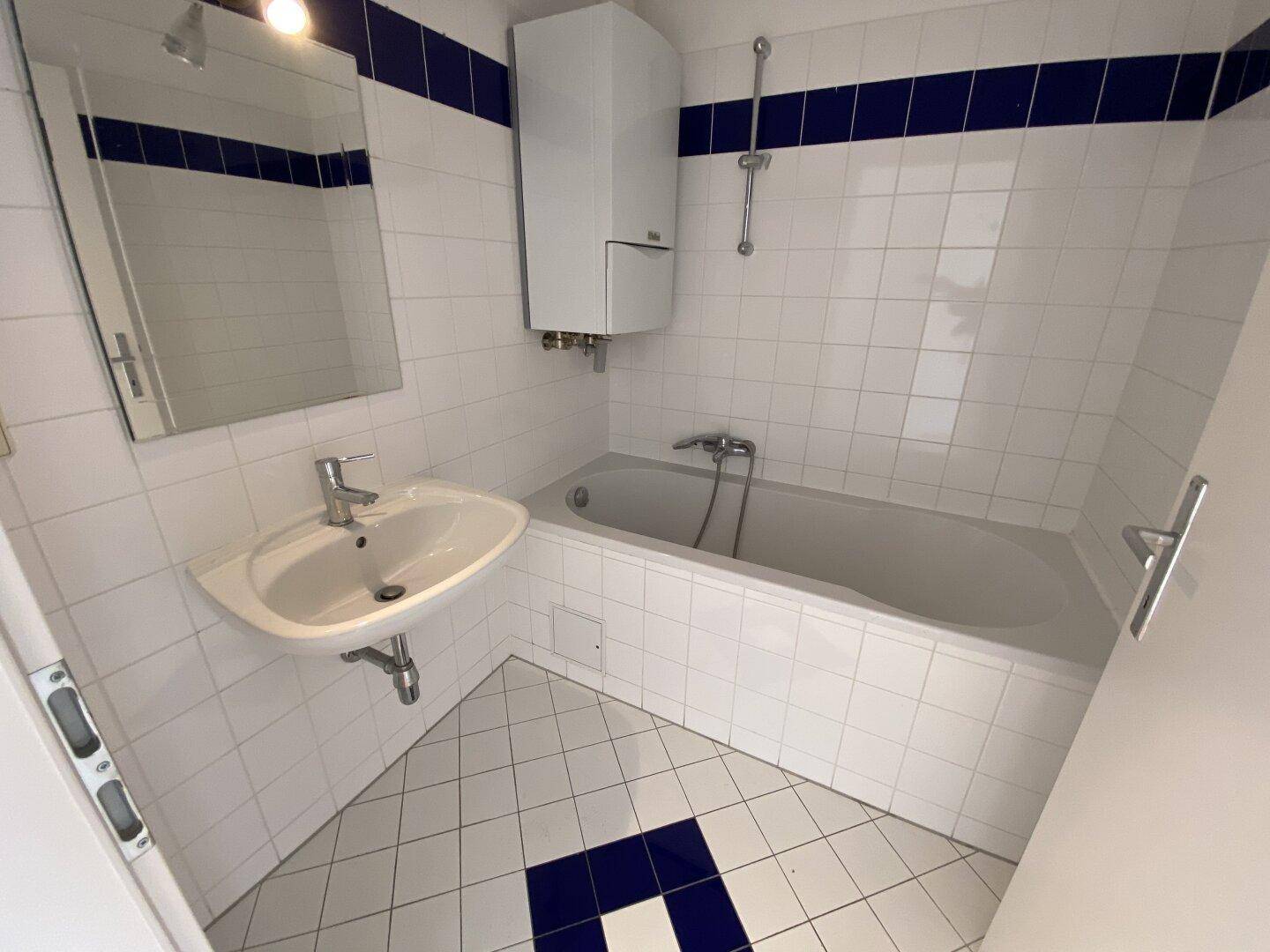 Gefliestes Badezimmer mit Badewanne, Waschbecken und einem Spiegelschrank, akzentuiert mit blauen Fliesen.